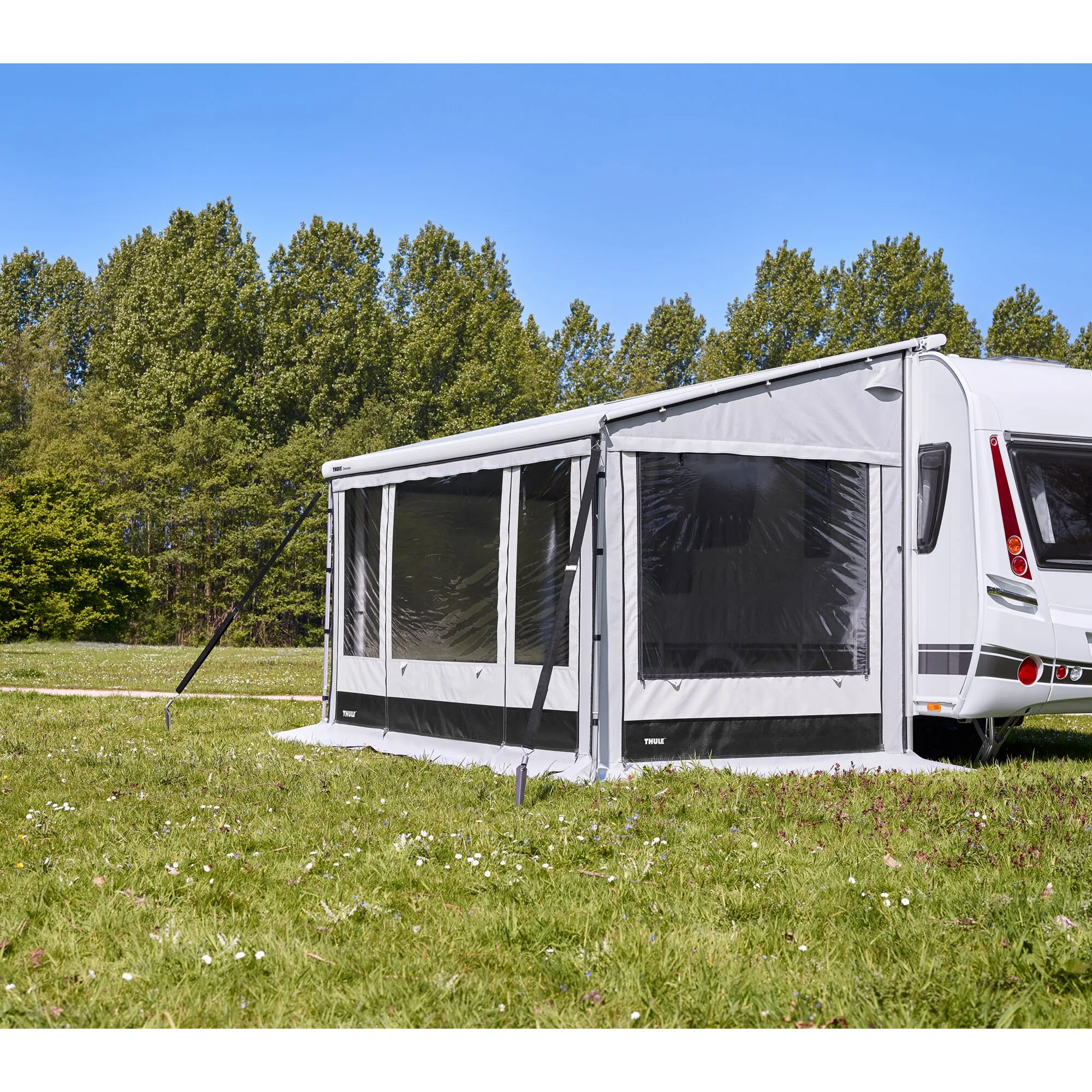Wohnwagen mit grauem Thule-Vorzelt, das durch schwarze Abspannbänder des Thule Hold Down Side Strap Kits im Gras gesichert ist