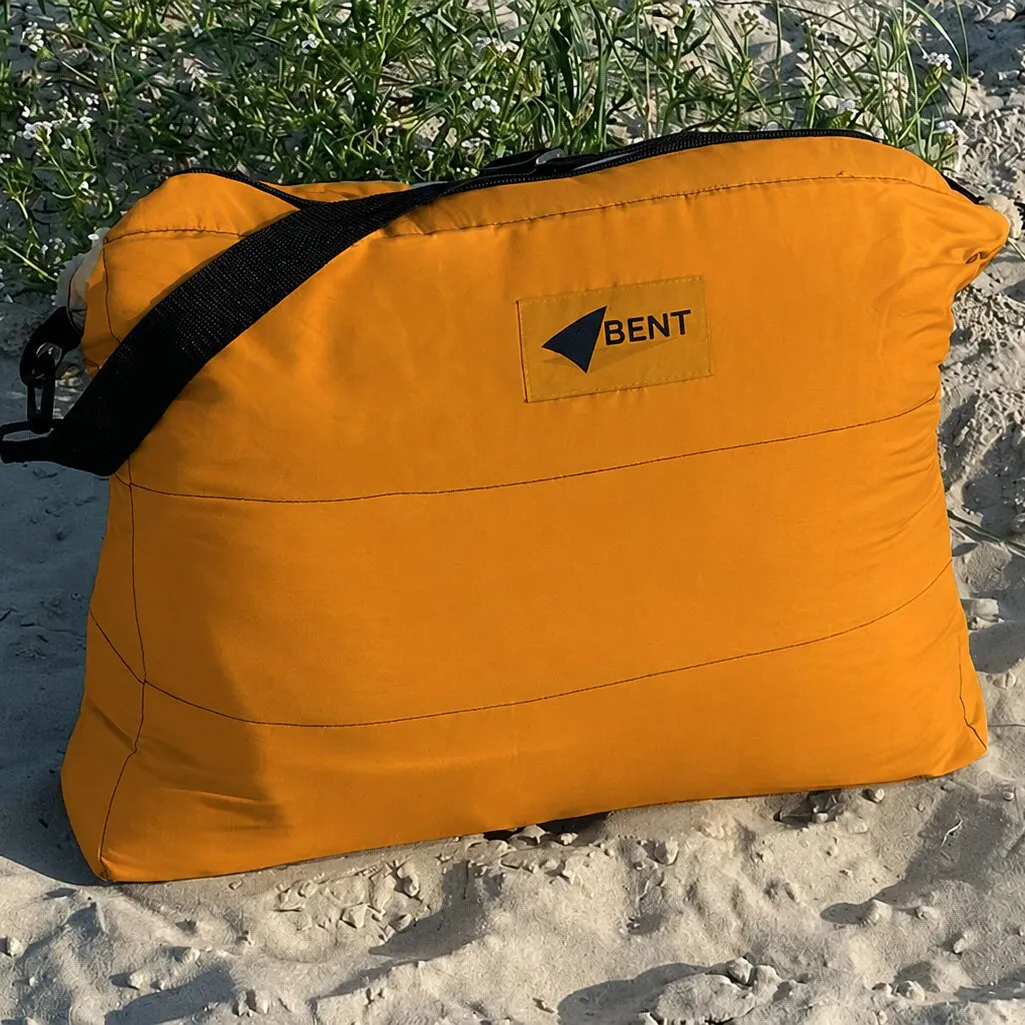 Oranger Vanlife-Schlafsack Bentcho im Leo-Design mit schwarzem Tragegurt und Bent-Logo auf sandigem Untergrund