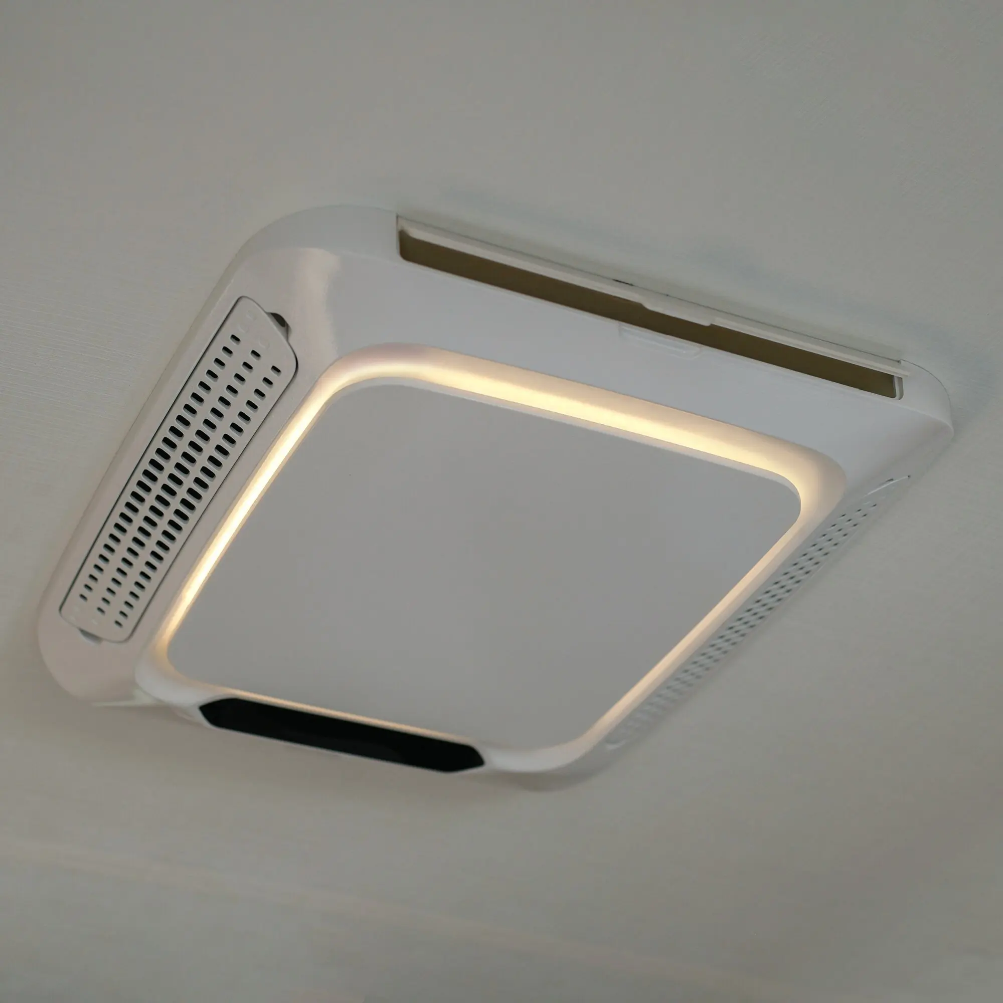 Weißes Deckenmodul mit integrierter LED-Ringbeleuchtung um eine Leuchte; links sichtbar ein rechteckiger Luftverteiler mit Lochgitter