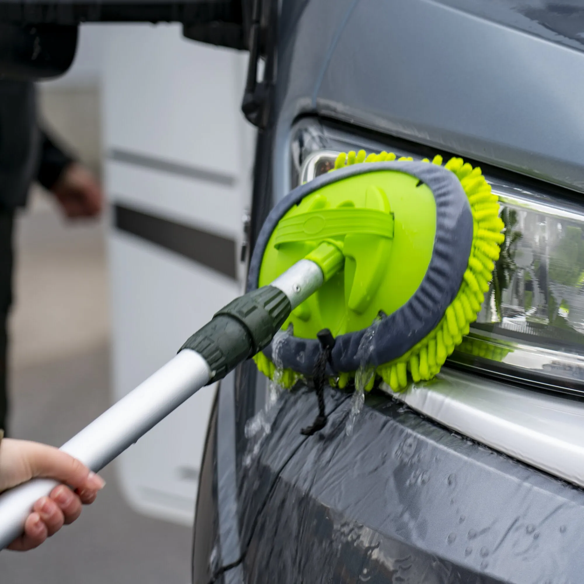 Grüner Mopp-Aufsatz mit grauen Mikrofaserfransen reinigt eine geöffnete Autotür, während Wasser abläuft
