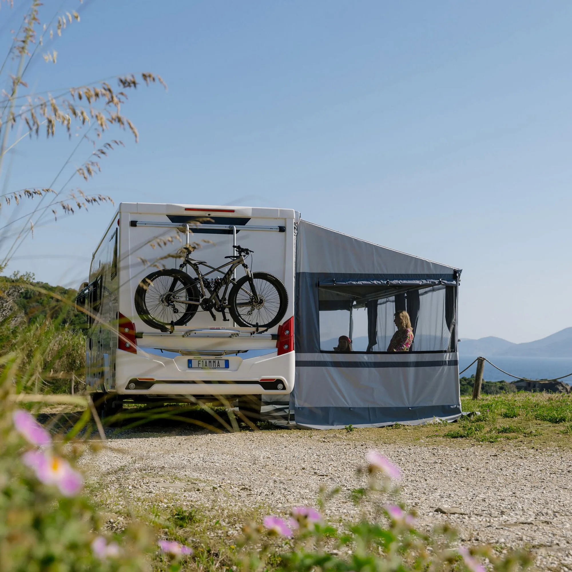 Graues Privacy Room Light F80s 300 High als Vorzelt an einem Wohnmobil mit Fahrrädern und geöffneter Seitenwand am Meer
