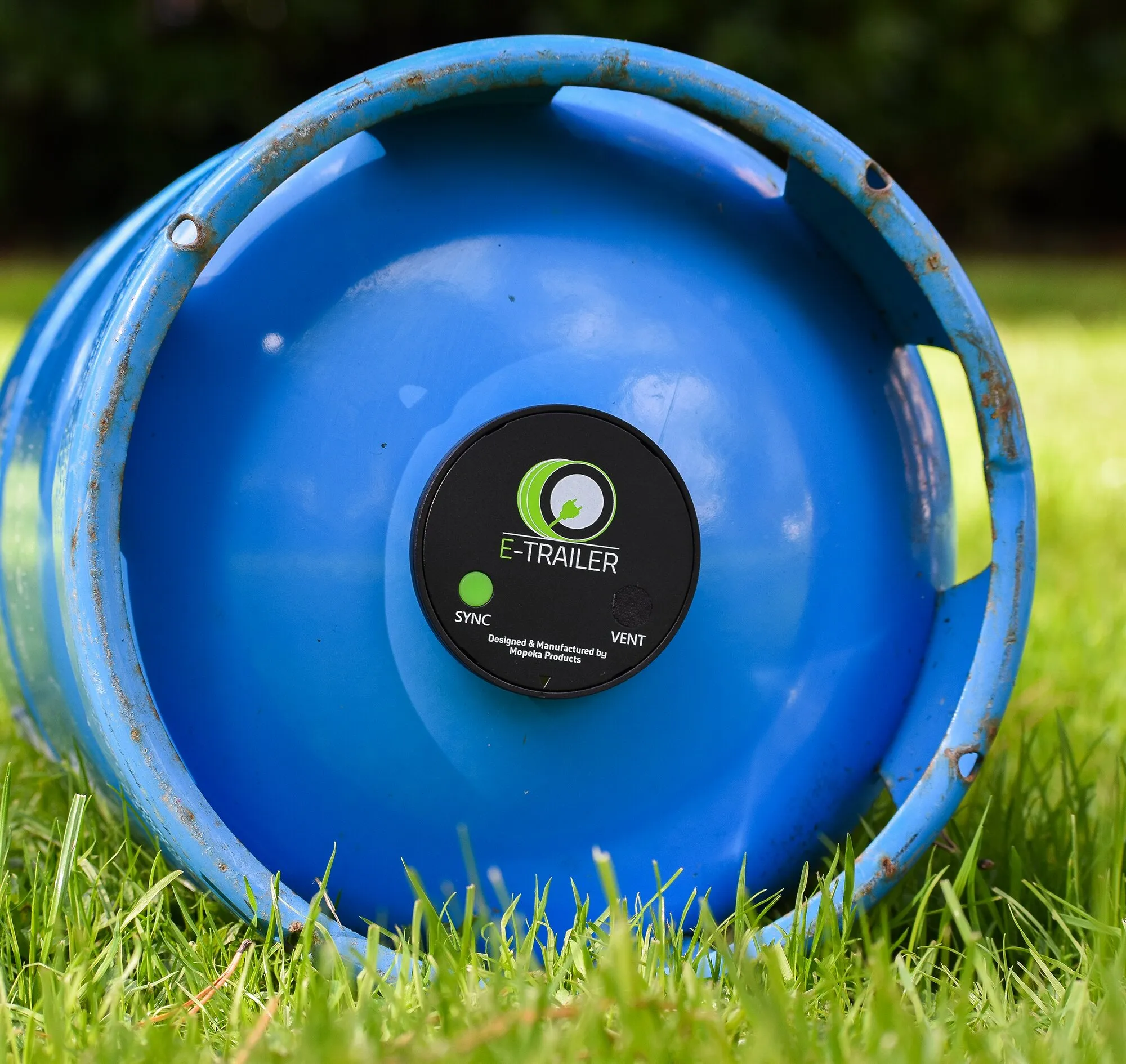 Blaue Gasflasche mit aufgesetzter runder E-Gaslevel-Füllstandsanzeige von E-Trailer, im Gras liegend