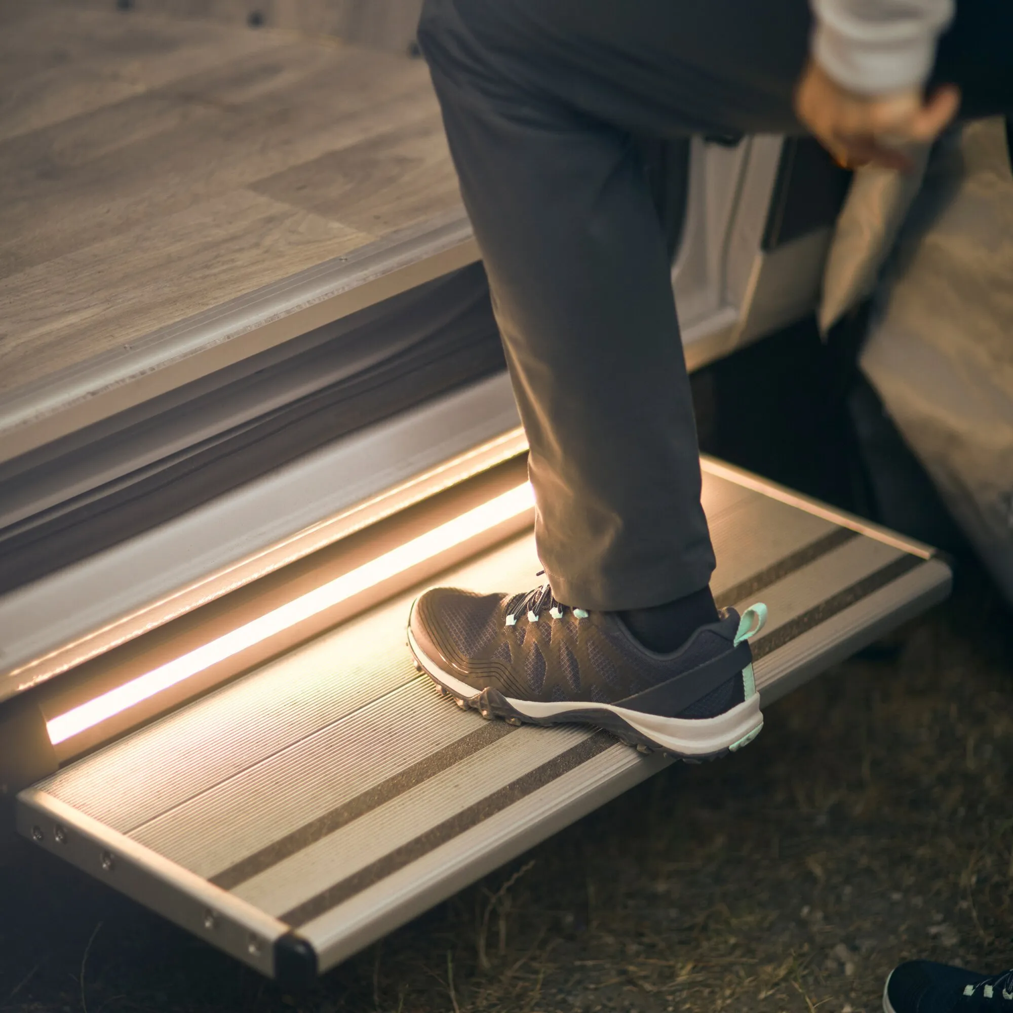 Eine Person betritt die ausgefahrene Trittstufe Thule Slide-Out Step G2 12V 407 mm an einem Fahrzeug mit strukturierter Aluminiumfläche