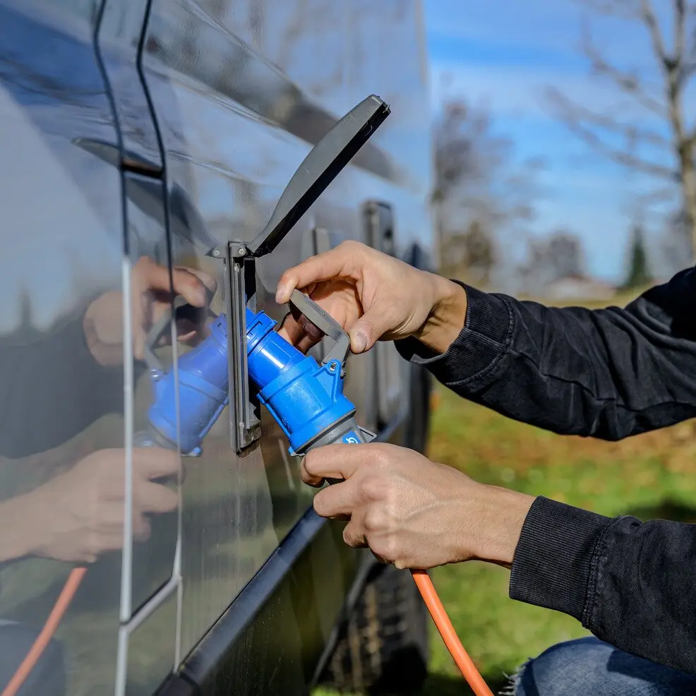 Orangefarbenes CEE-Verlängerungskabel (5 m) mit blauer Industriesteckverbindung wird von einer Person an eine Fahrzeugsteckdose angeschlossen