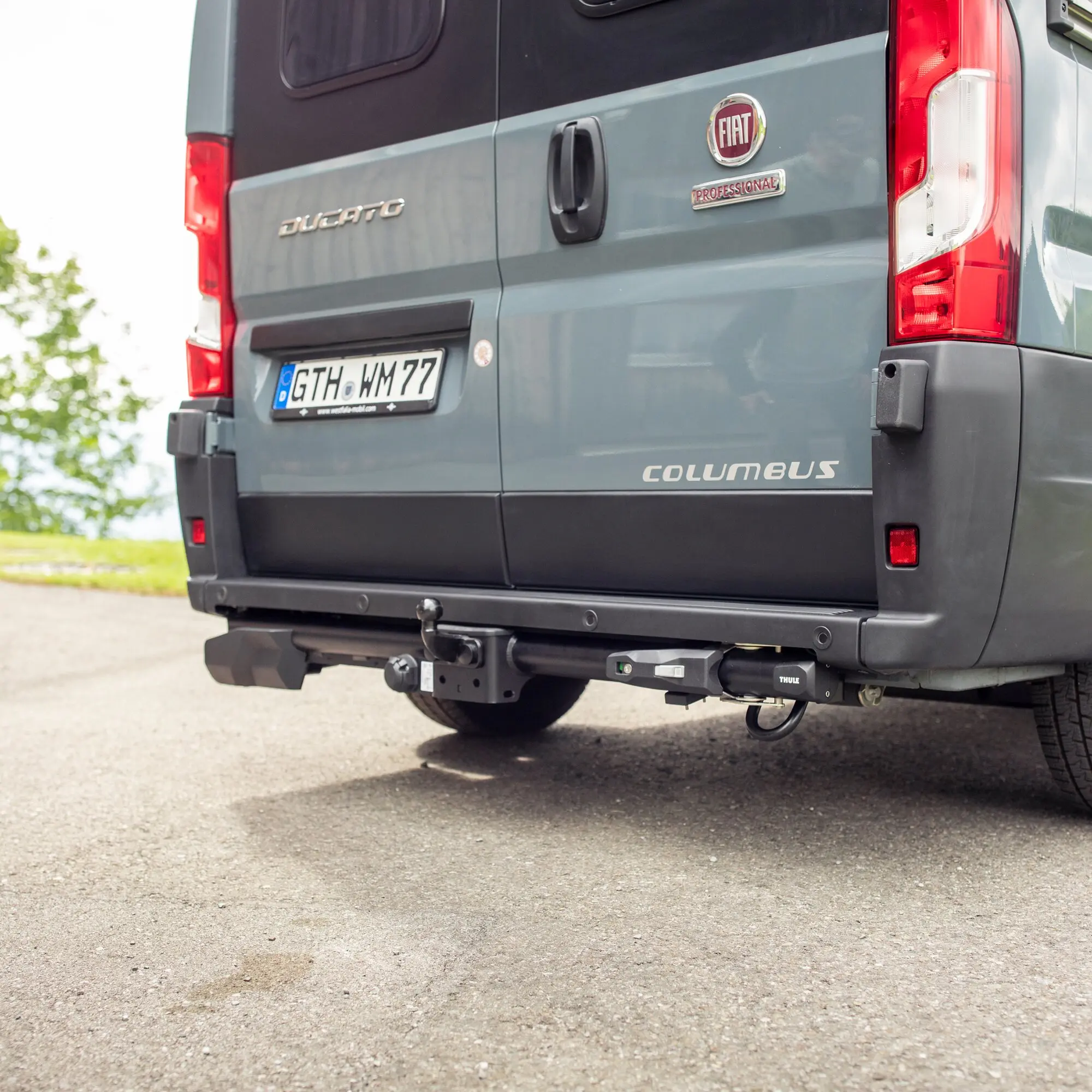 Rückseite eines grauen Fiat Ducato mit Fiat-Logo und Columbus-Schriftzug untere Stoßstangenabdeckung und Thule VeloSwing Halterung am Heck