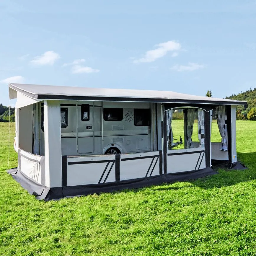 Graues Dauervorzelt Allgäu 300 mit Fenstern und transparenten Seitenwänden an einem Wohnwagen auf einer Wiese