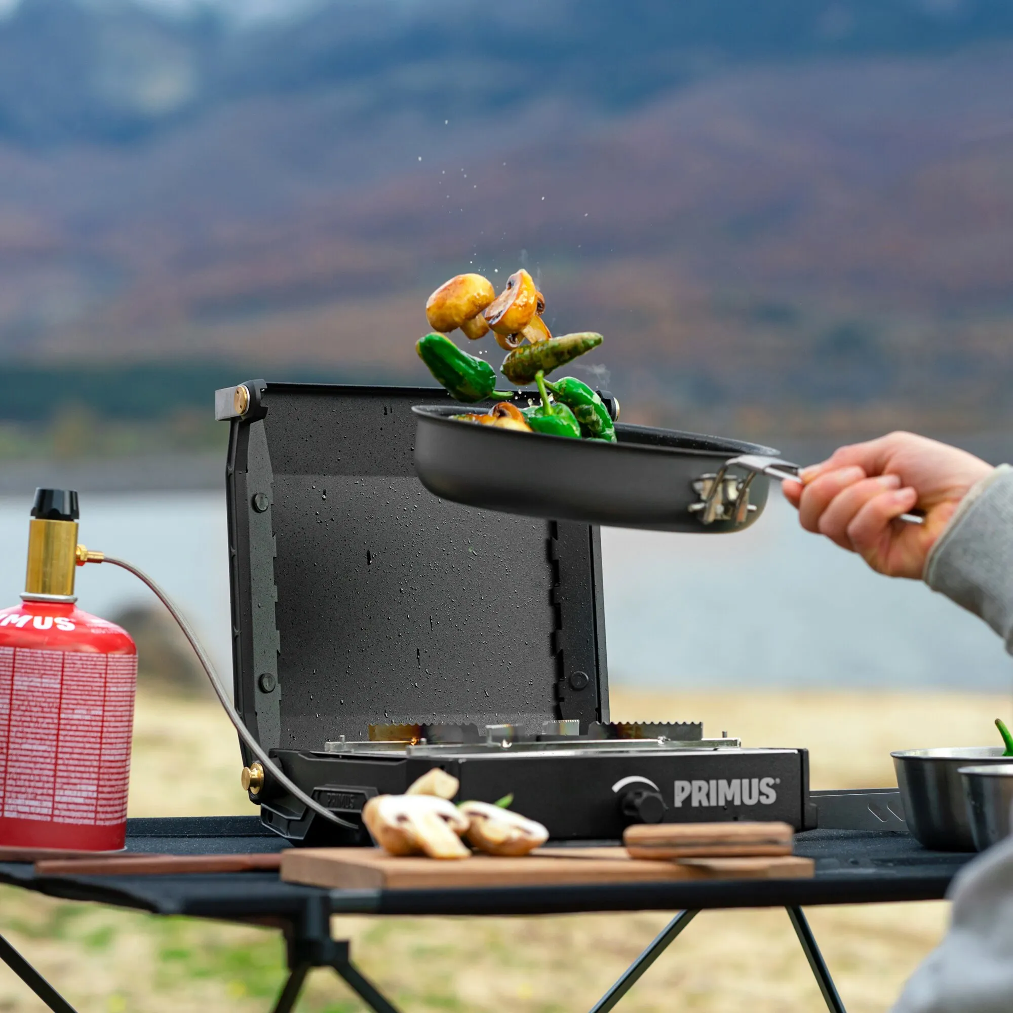 Schwarzer Primus Moja Stove Gaskocher mit angeschlossener Gasflasche, auf dem eine Pfanne mit Pilzen und Paprika erhitzt wird