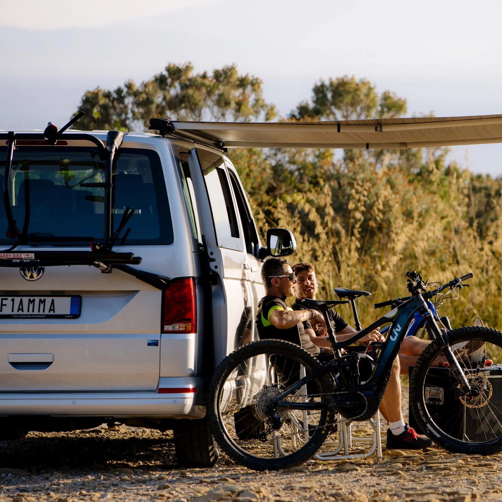 Weißer VW-Van mit Heck-Fahrradträger Carry-Bike, zwei Mountainbikes am Träger befestigt, Outdoor-Szene auf kiesigem Untergrund