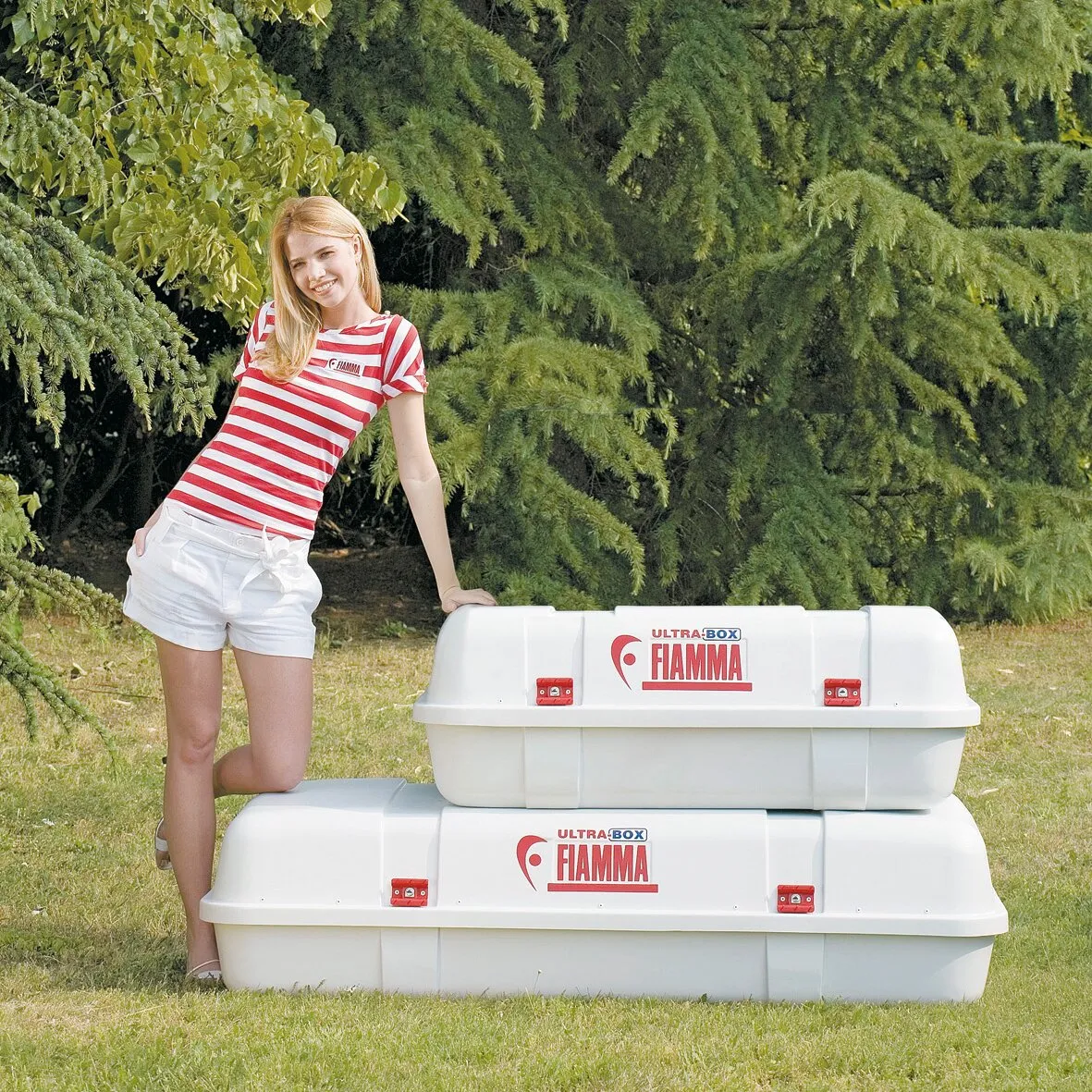 Zwei weiße Fiamma Ultra-Boxen im Garten, darunter eine Dachbox Ultra Box Top mit 400 Litern Volumen und rotem Verschlussbeschlag