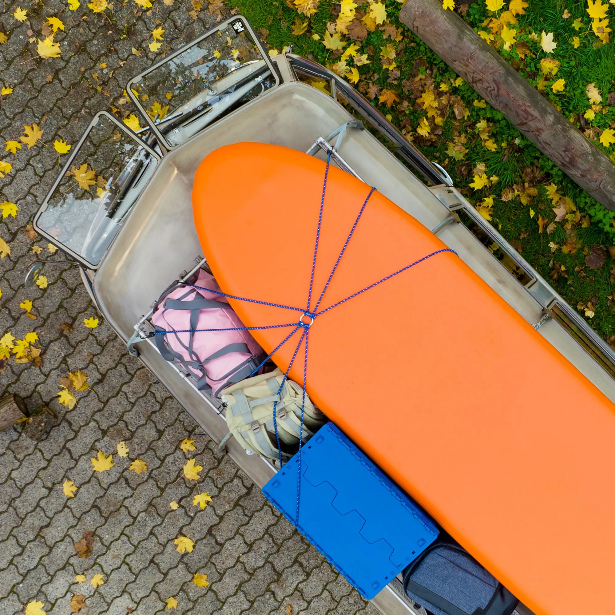 Blaue Gepäckspinne mit mehreren elastischen Schnüren sichert eine orangefarbene Transportbox auf einem offenen Fahrradanhänger