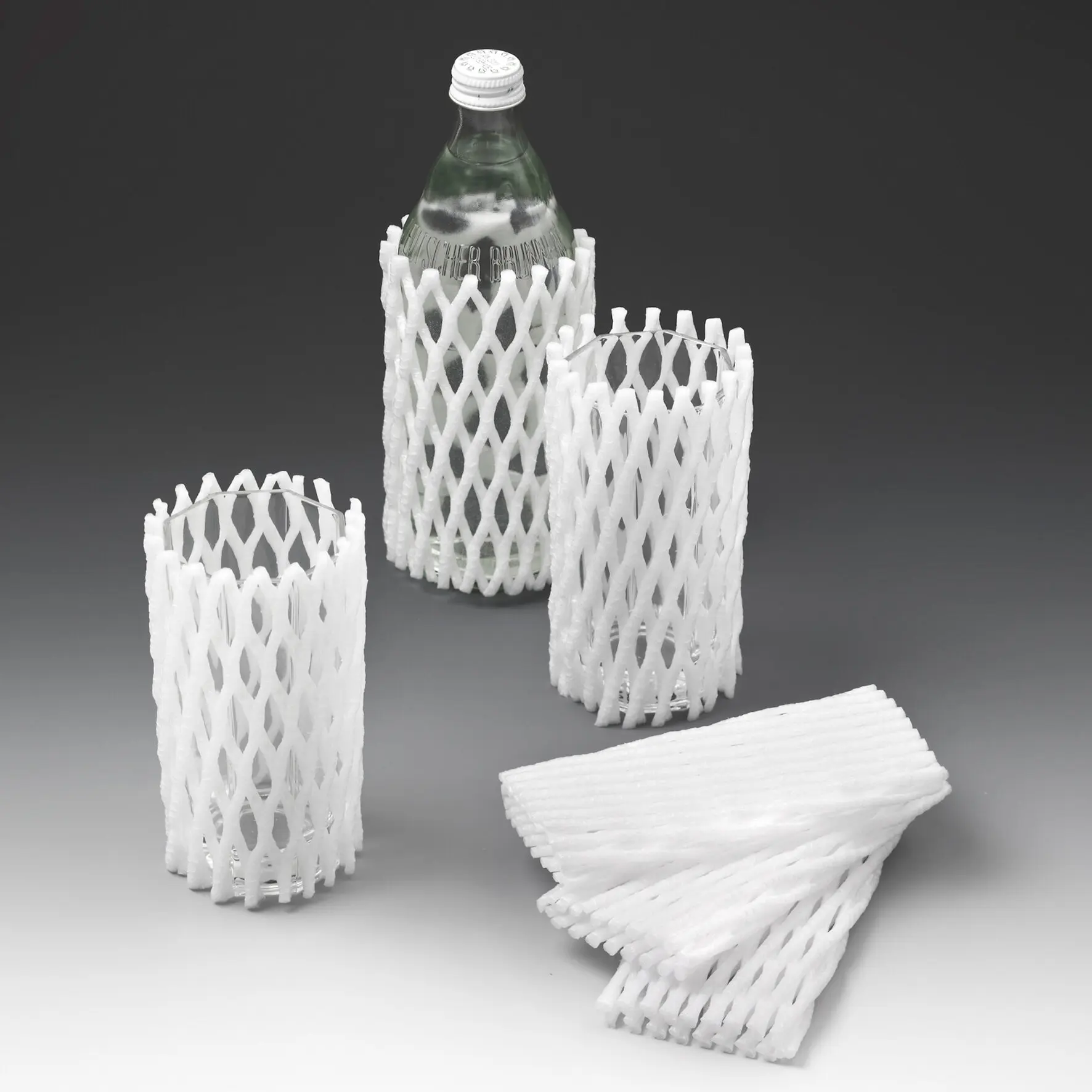 Mehrere weiße Schaumstoff-Netzschutzhüllen um Glasflaschen; zentrale Flasche in Glas- und Porzellanschutznetz, grauer Hintergrund