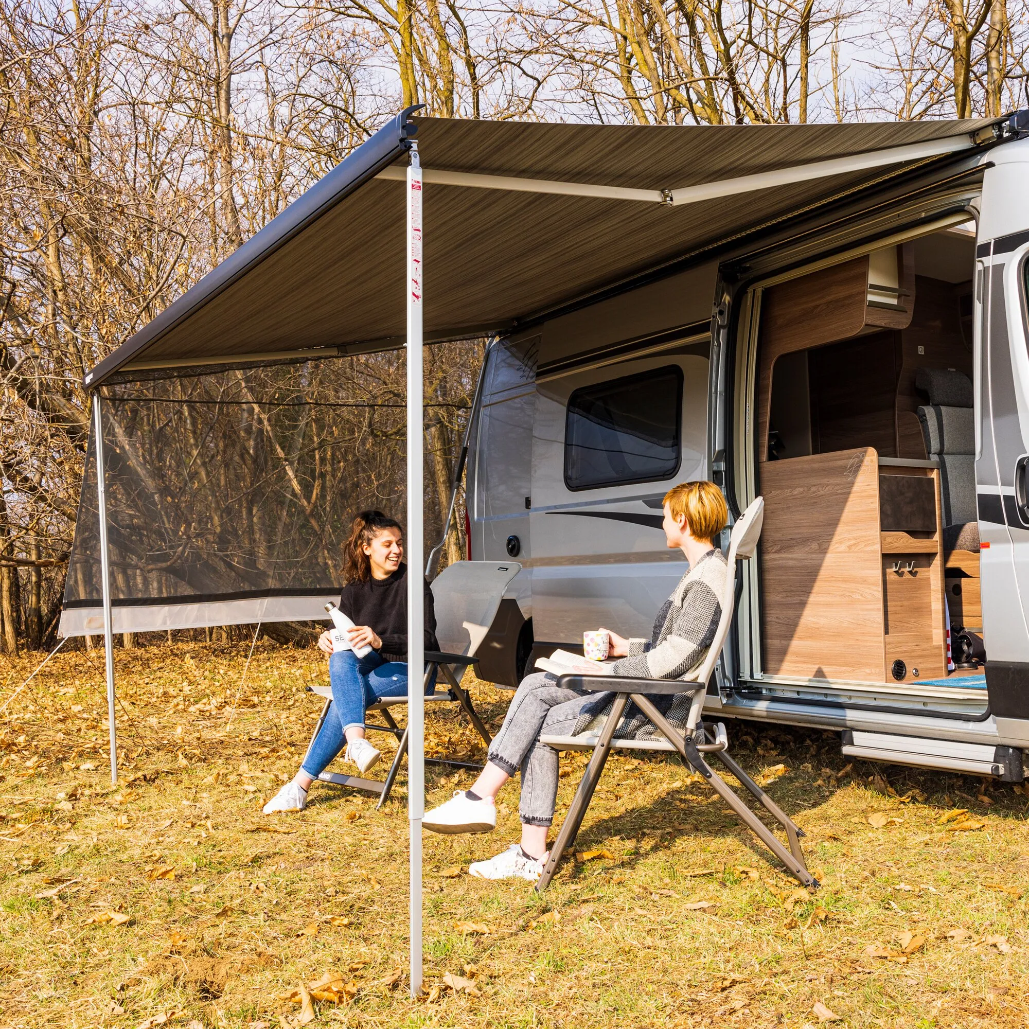 Ausfahrbare Markise am Wohnmobil mit transparenter Sun View Side als Seitenwand; zwei Personen sitzen darunter im Freien