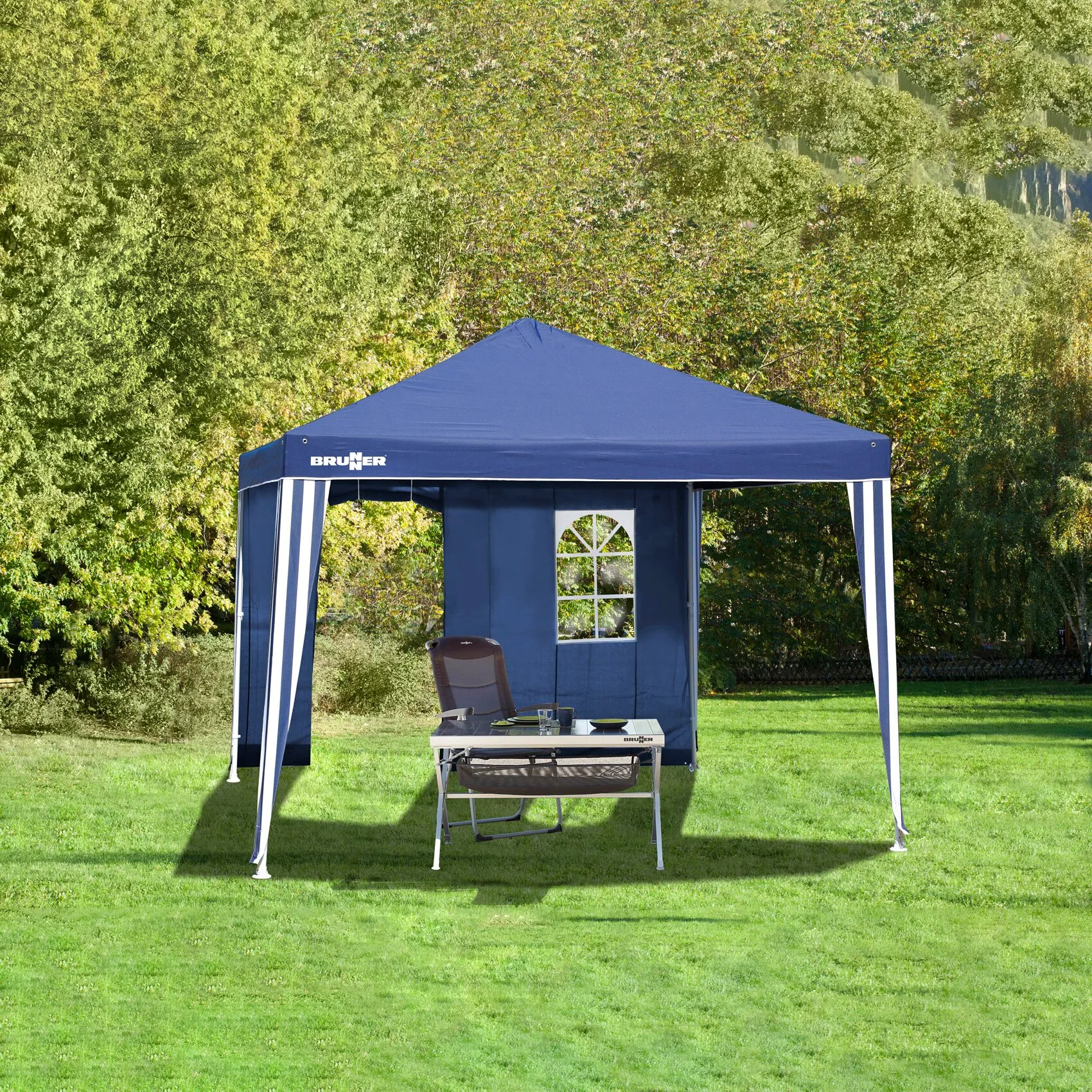 Blauer Gartenpavillon Isola II von Brunner mit Seitenwand, Tür und Fenster auf einer Wiese, ausgestattet mit Tisch und Stühlen