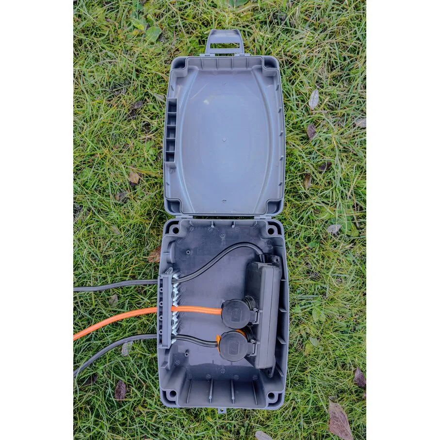 Geöffnete graue Wetterschutz-Box IP54 mit Kabelanschlüssen und zwei Steckdosen, auf einer Wiese liegend