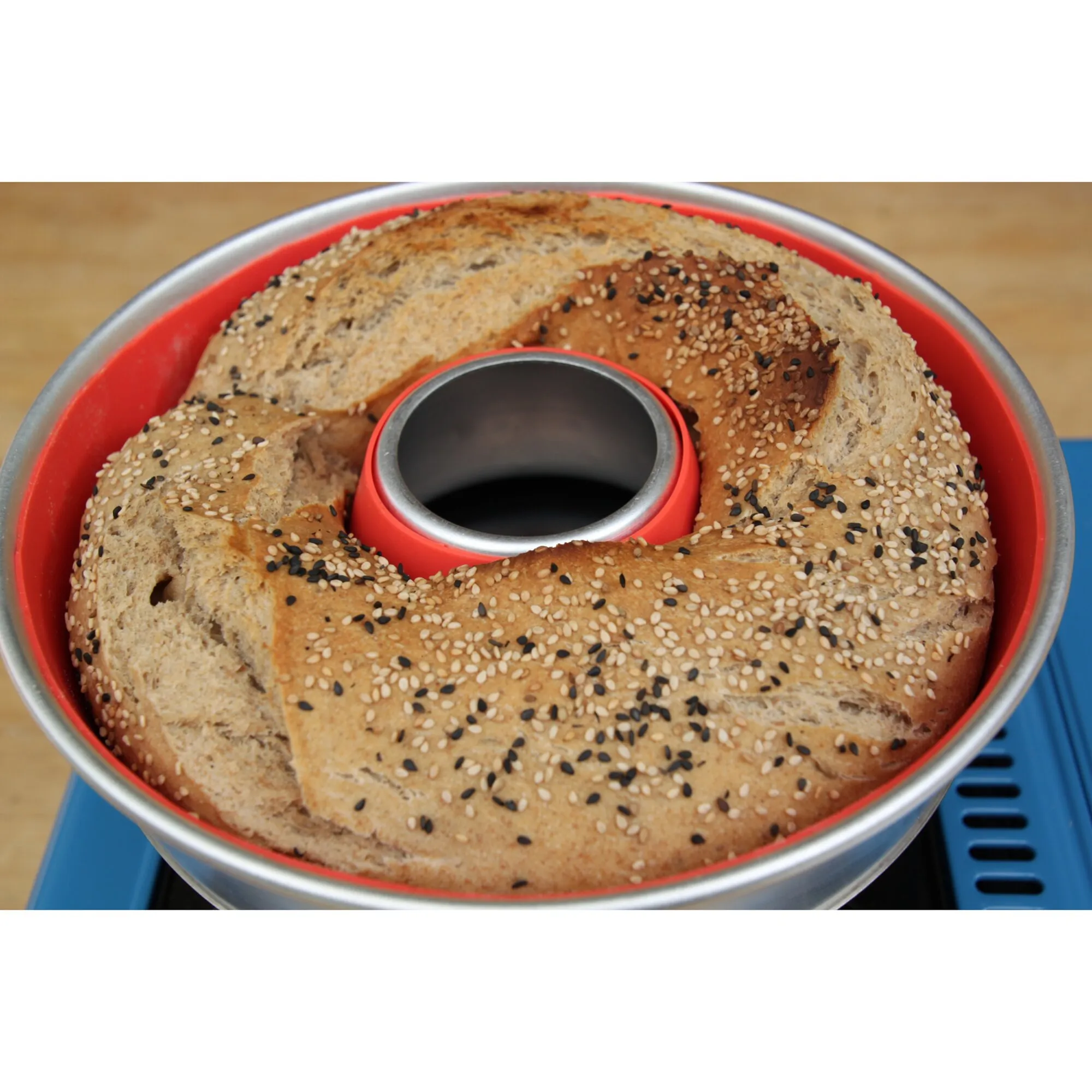 Rote Silikonform mit Metallrand und Mittelsteg, gefüllt mit gebackenem, mit Sesam bestreutem Ringbrot