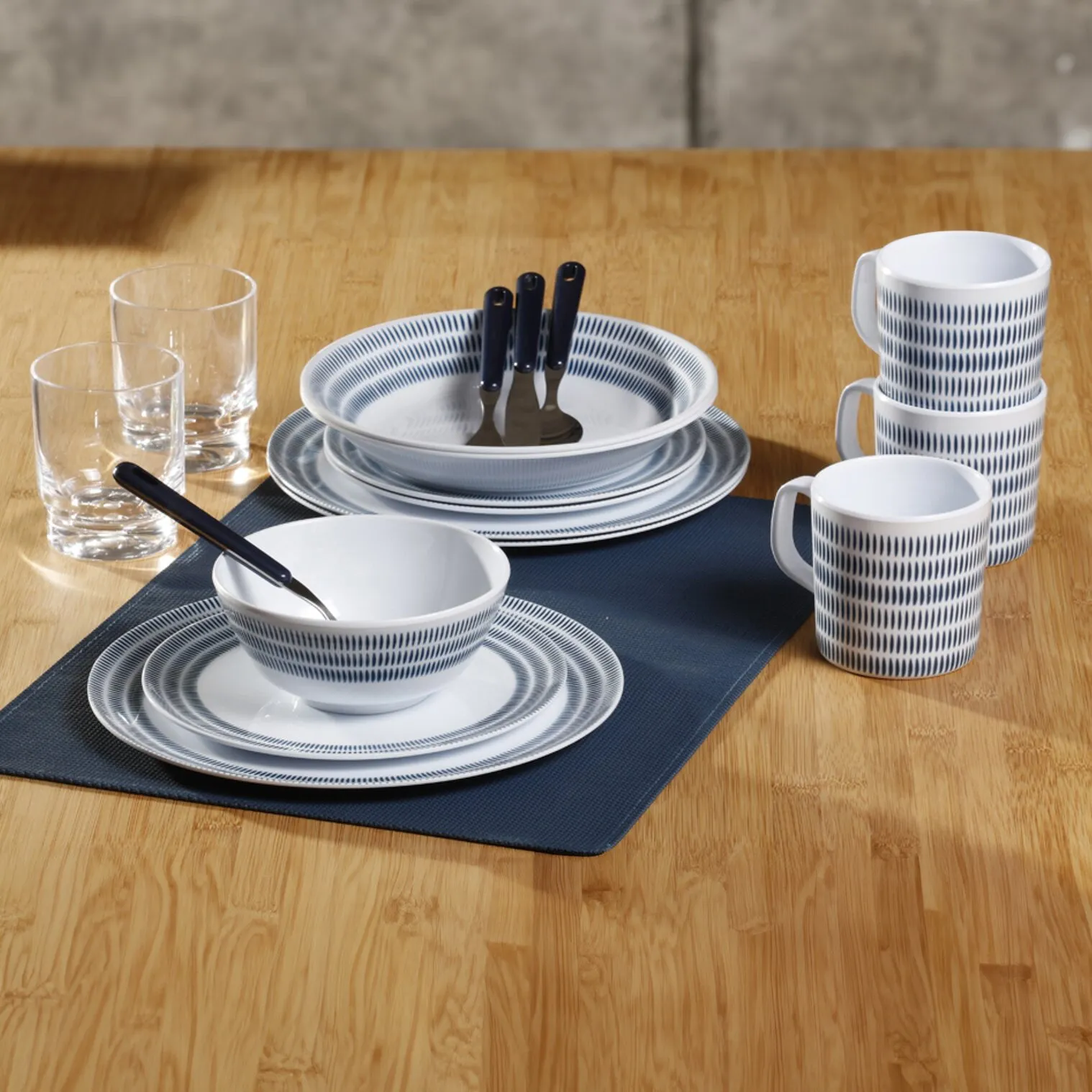 Geschirrset Bluebay mit weiß-blau gemusterten Tellern, Schalen und Tassen, Besteck und Gläsern auf einem gedeckten Tisch