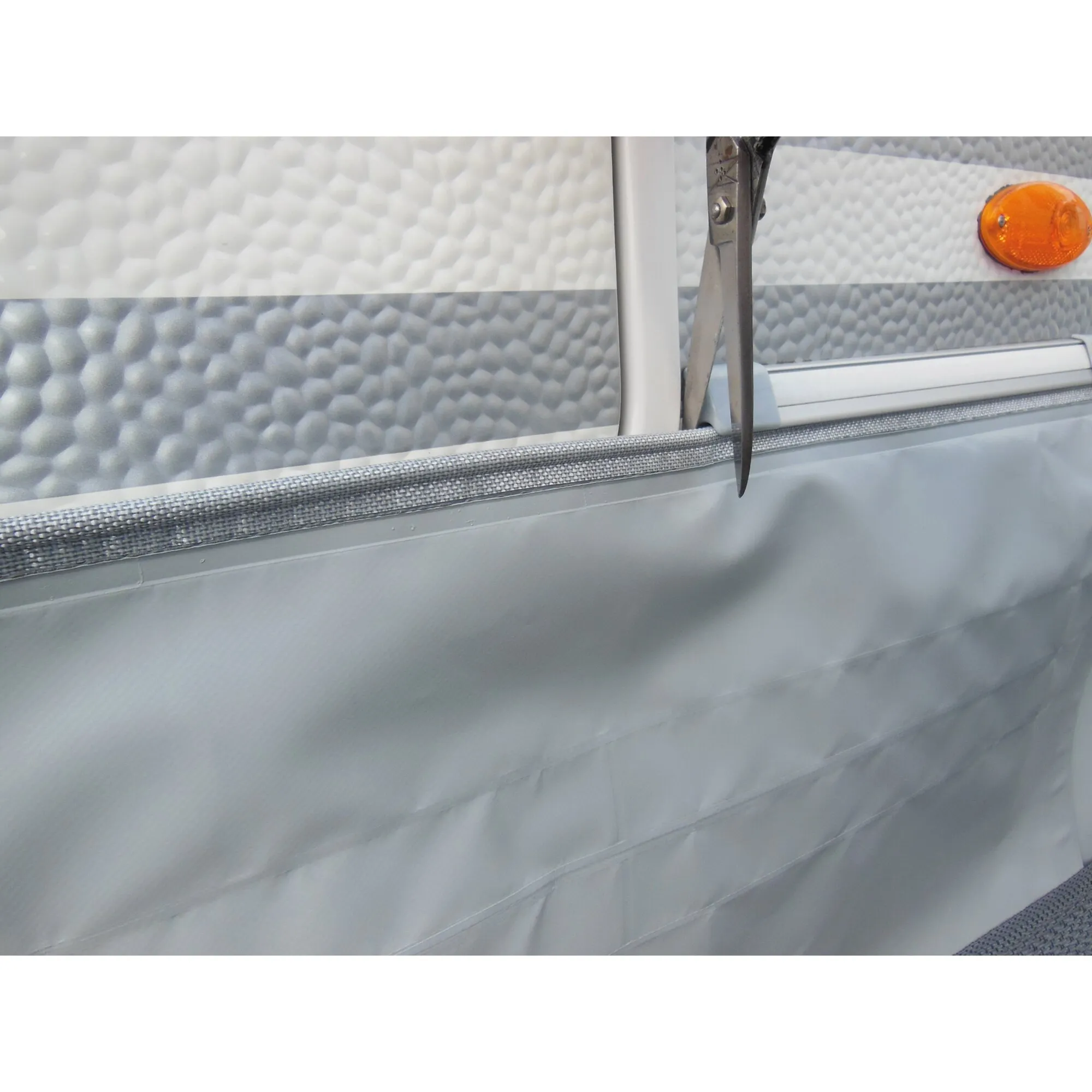 Detailaufnahme des Befestigungssets für eine graue Bodenschürze am weißen Wohnwagen mit abgesenktem Türeinstieg