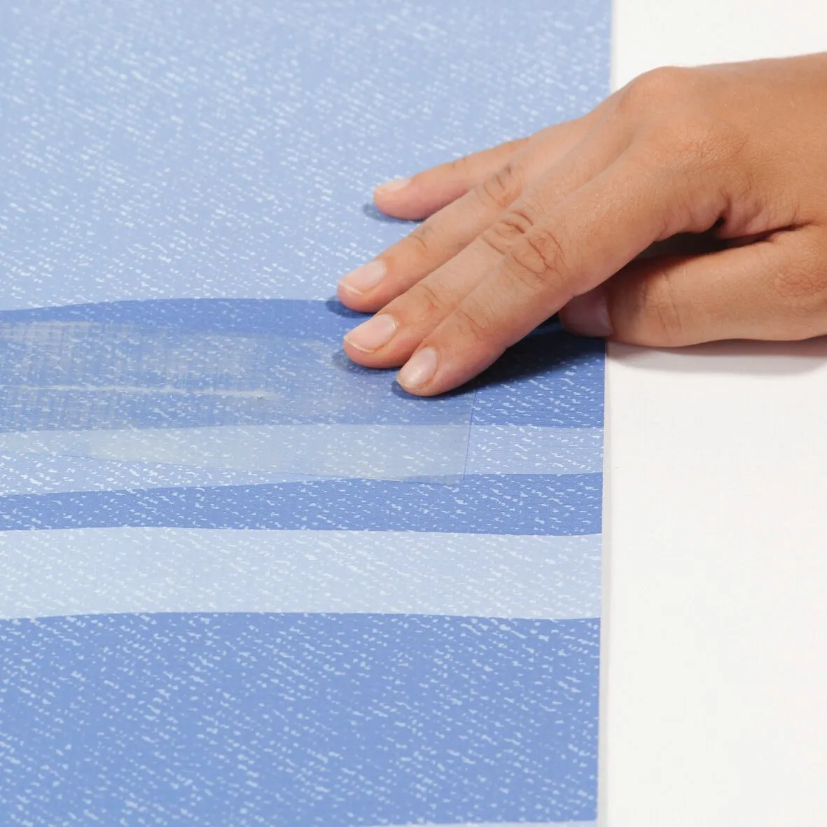 Hand glättet eine transparente Reparaturfolie auf einem blau gemusterten Bodenbelag des Kit Repair Plus