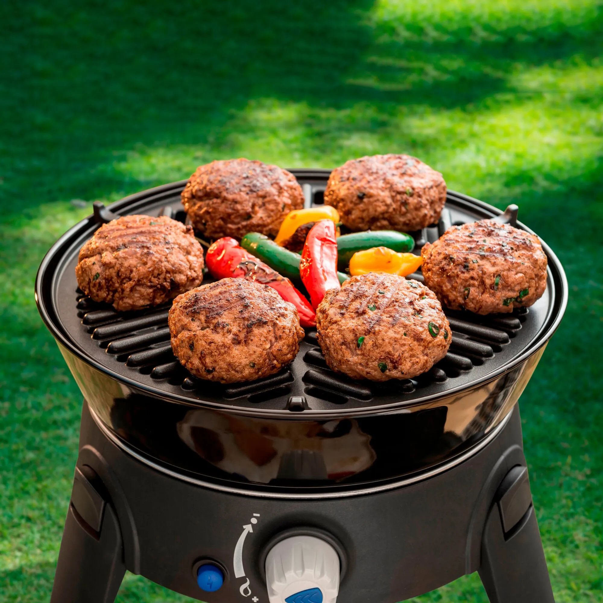 Schwarzer Gasgrill Safari Chef 30 mit sechs gegrillten Burgerpatties und bunten Paprikaschoten auf dem Rost im Garten