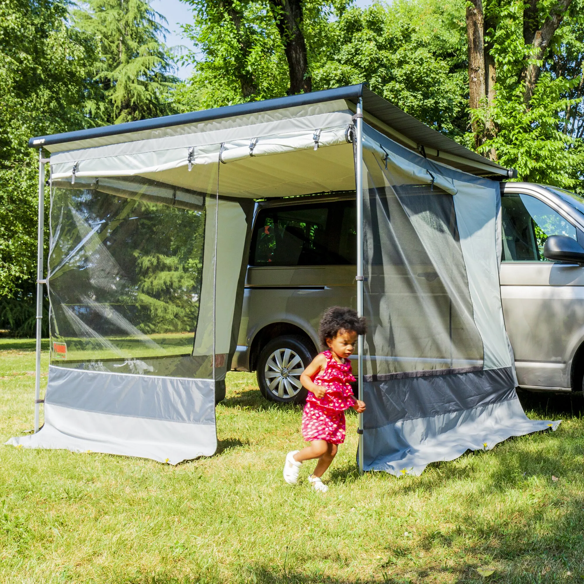 Graues Markisenzelt Room Van für einen Van mit transparenten Seitenwänden, aufgebaut auf einer Wiese; ein Kind läuft davor entlang