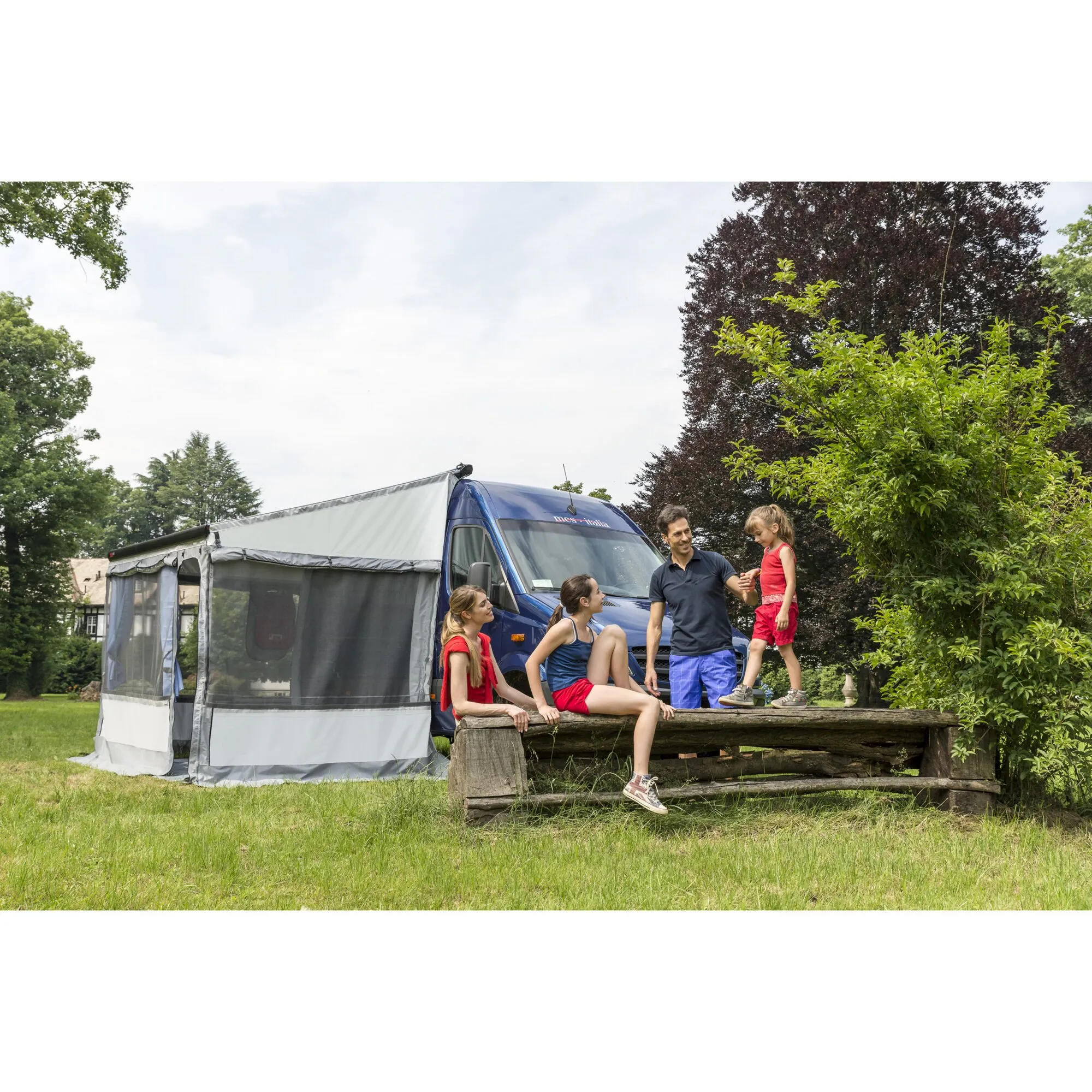 Blaues Reisemobil mit grauer Frontwanderweiterung 125 und einer Familie beim Camping im Grünen