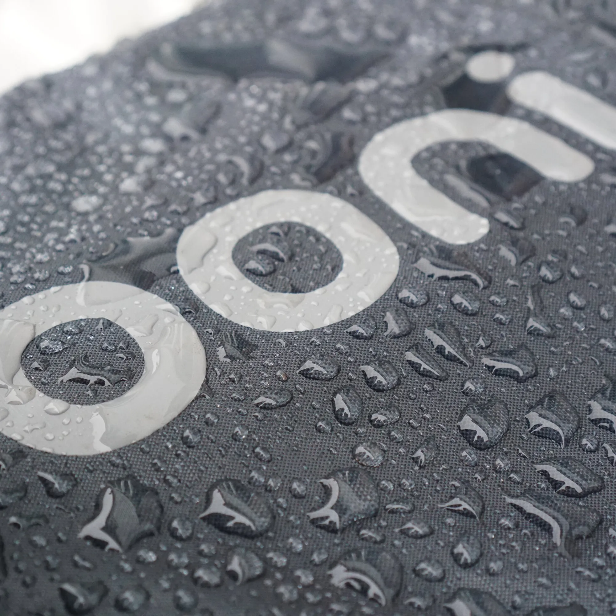 Detailaufnahme der dunkelgrauen Tragetasche Ooni Koda 12 mit großem hellgrauem Ooni-Logo und Wassertropfen auf dem Stoff