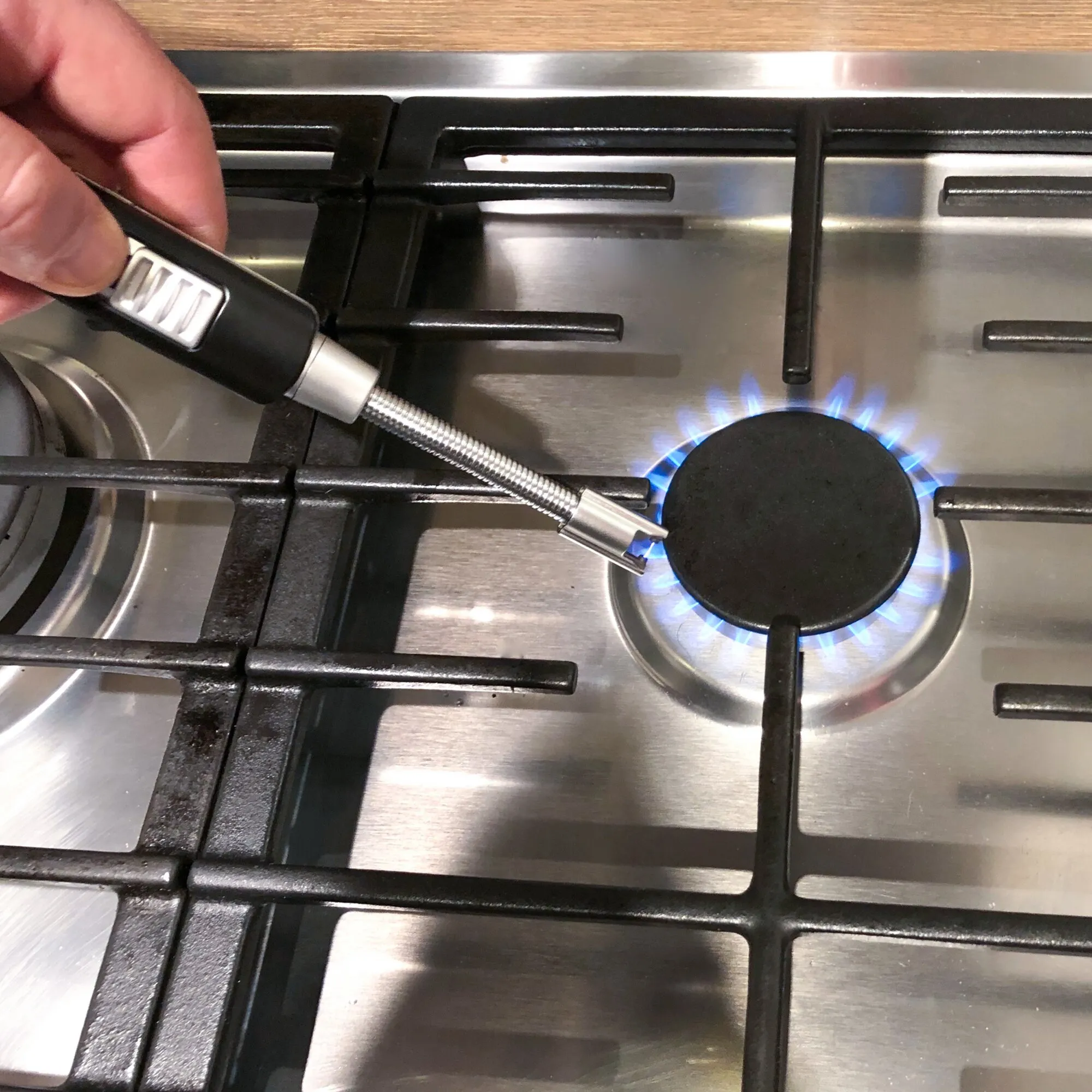 Hand hält ein schwarzes elektronisches Stabfeuerzeug mit flexiblem Metallhals über einem eingeschalteten Gasherd