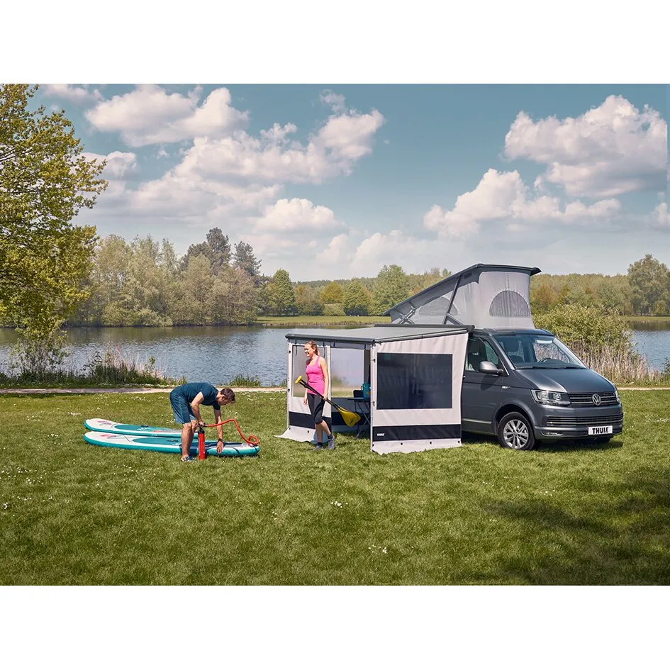 Rain Blocker Set an einem grauen Minivan mit seitlicher geschlossener Kabine am See, daneben zwei Personen und Stand-up-Paddleboards