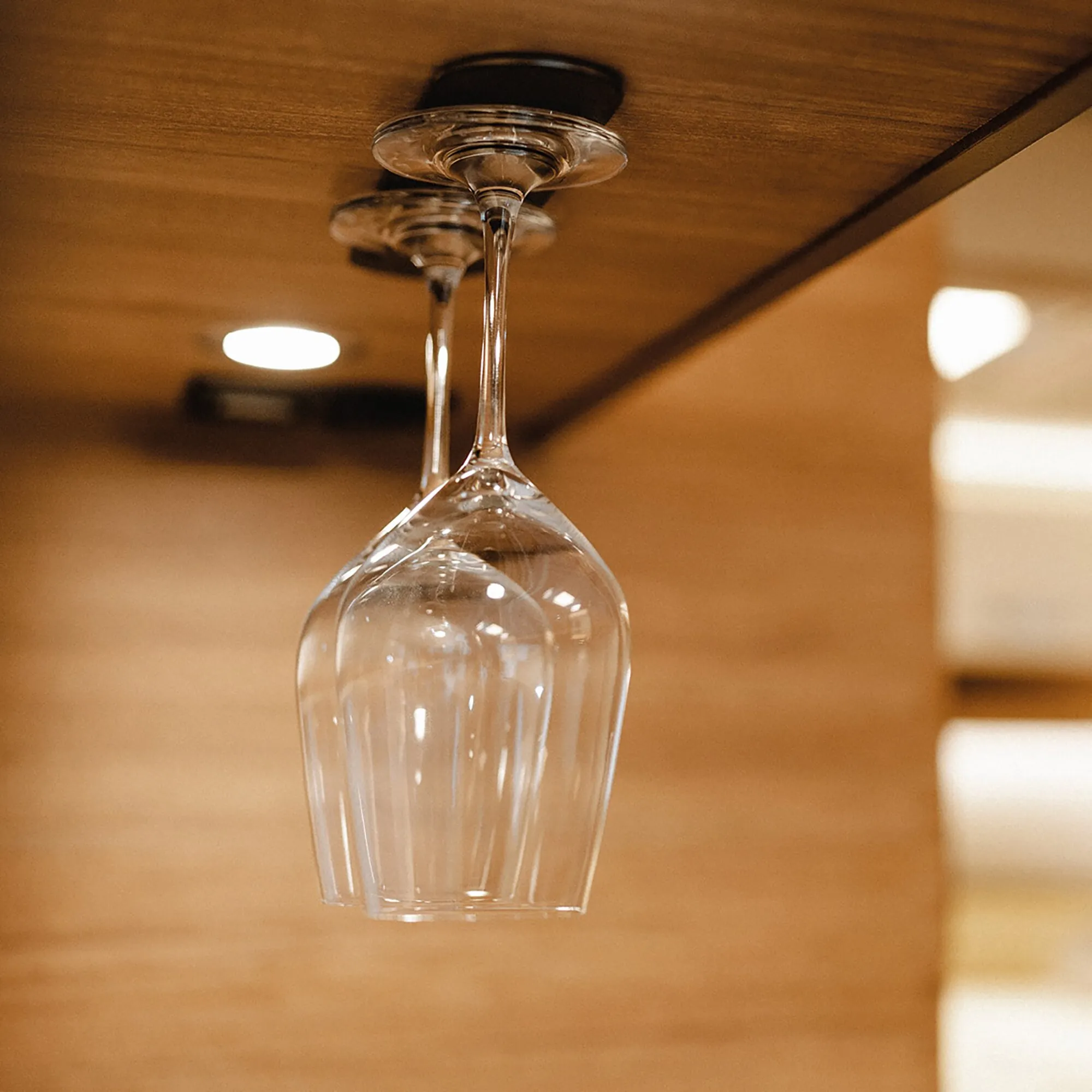 Transparentes Weinglas hängt kopfüber an einer Deckenhalterung in einem warm beleuchteten Innenraum