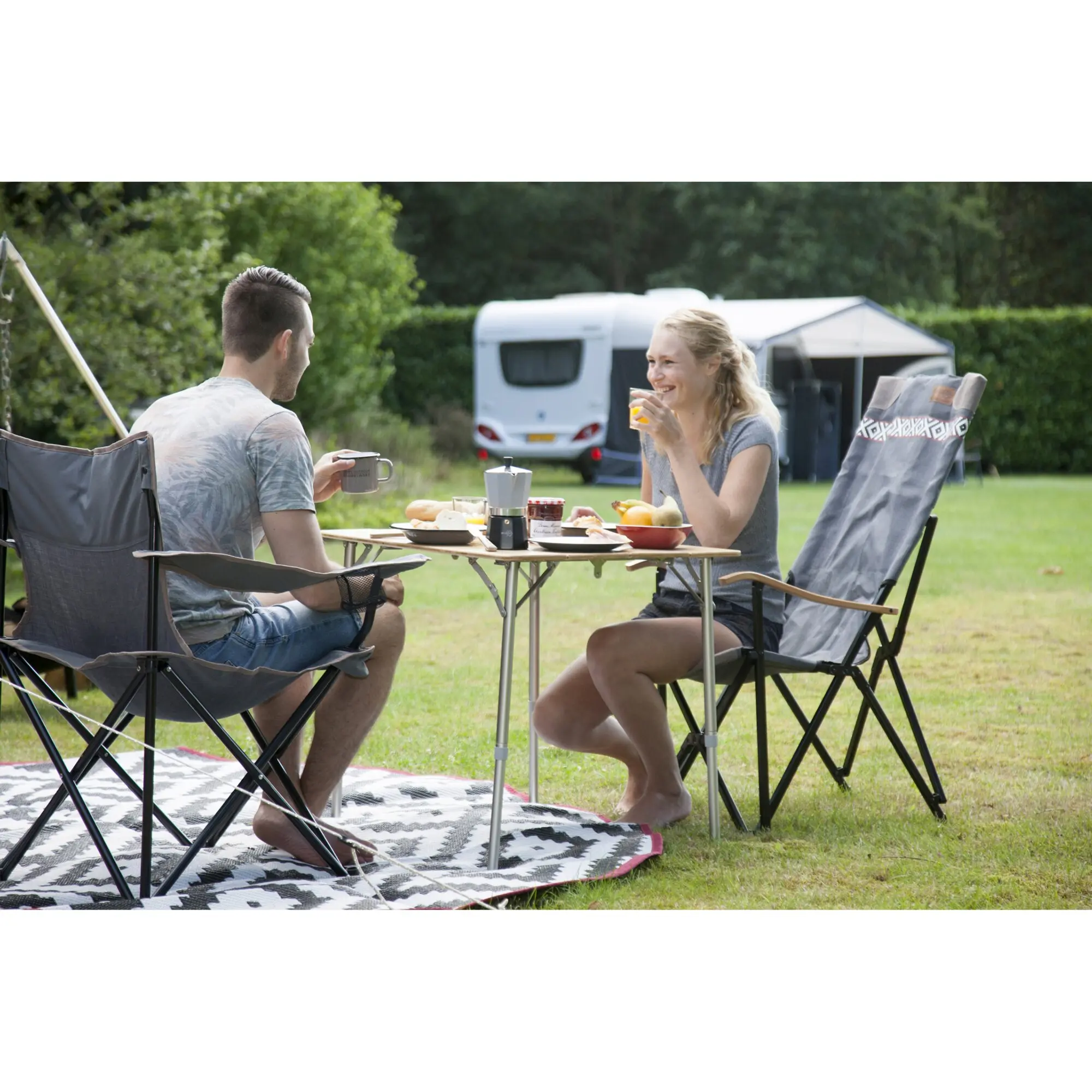 Zwei Personen sitzen an einem klappbaren Campingtisch Suffolk im Freien, frühstücken; Espressokocher, Obst und Marmelade stehen darauf