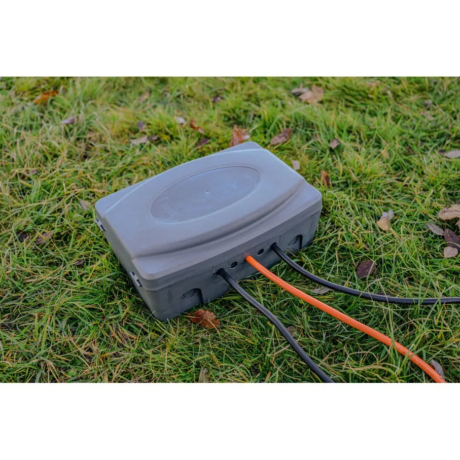 Graue Wetterschutz-Box IP54 mit geschlossenem Deckel auf einer Wiese, durch mehrere Kabelöffnungen führen schwarze und orange Kabel