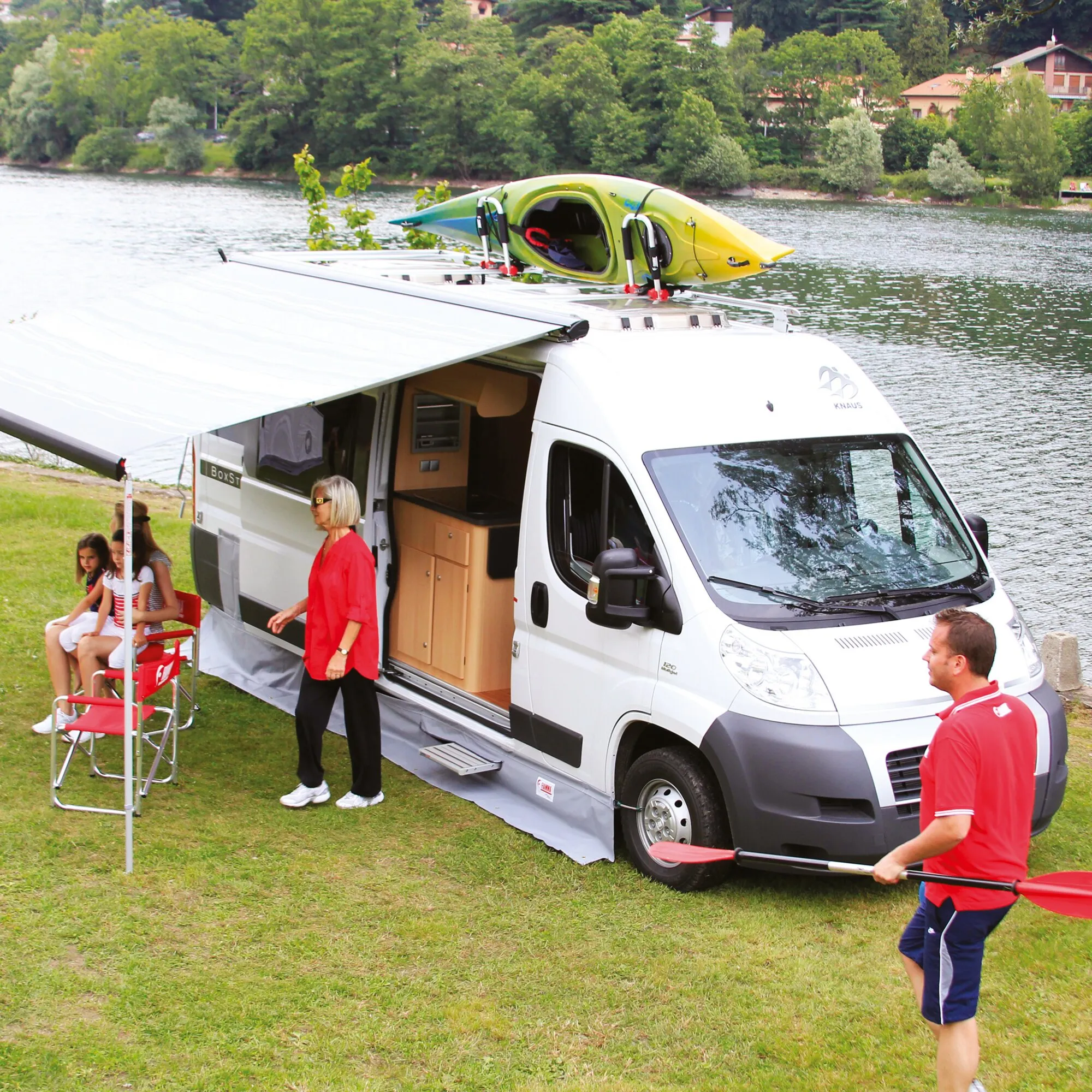 Graue Bodenschürze am weißen Fiat Ducato 250 auf einem Campingplatz am See, mit ausgefahrener Markise und Kajak auf dem Dach