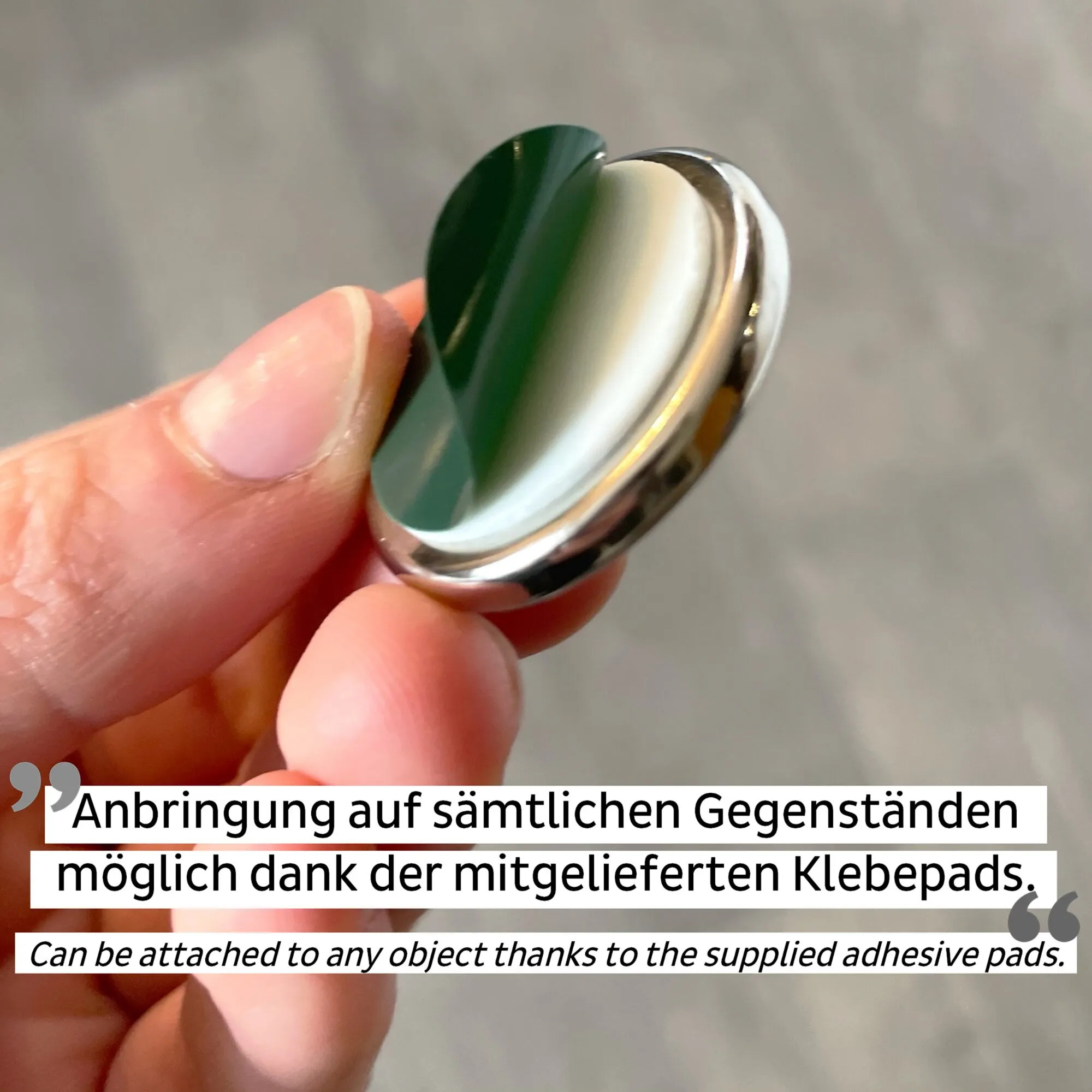 Runder silberner Power-Magnet mit grüner Klebefläche, zwischen zwei Fingern gehalten; Hinweis auf haftende Klebepads sichtbar