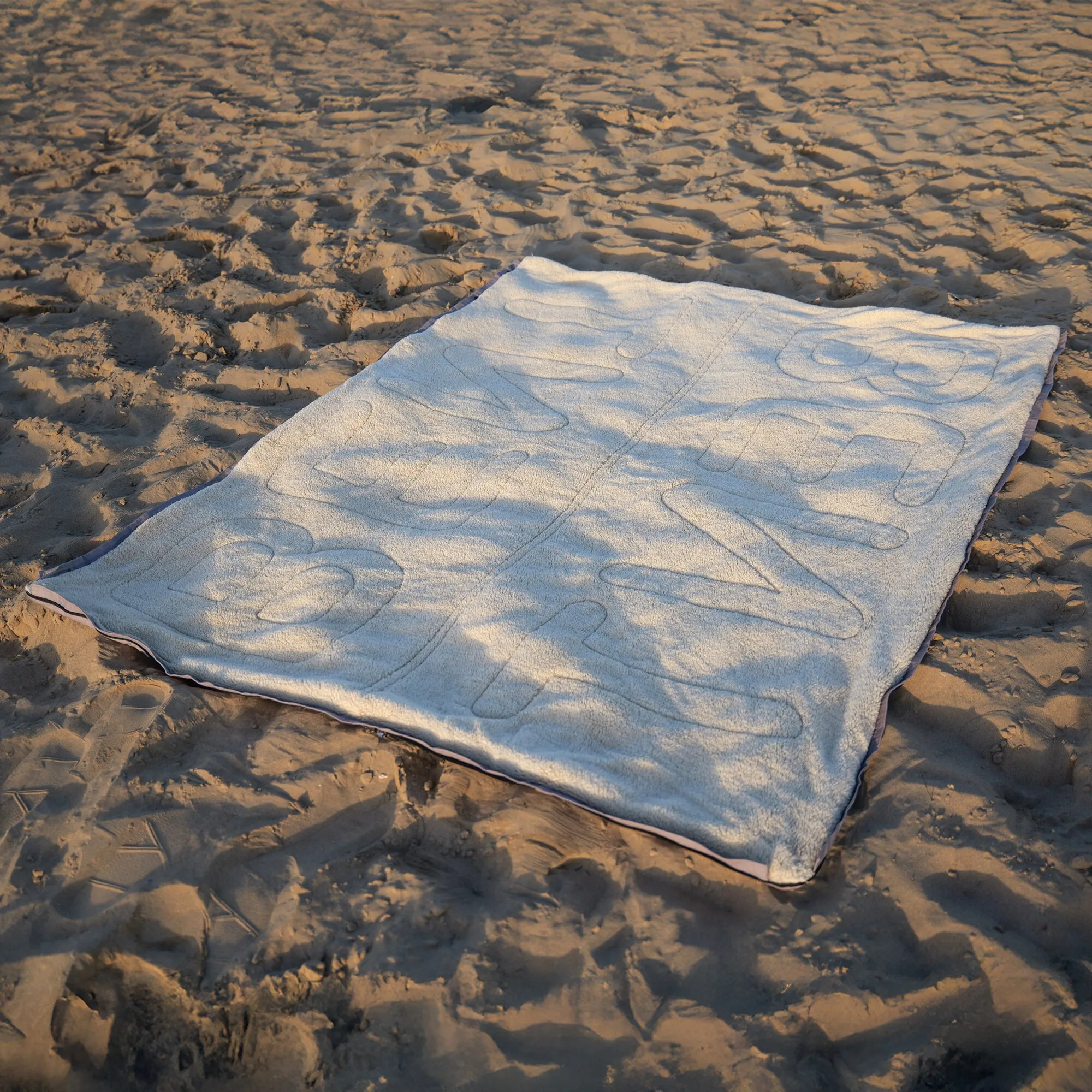 Grauer Vanlife-Schlafsack Bentcho ausgebreitet auf sandigem Strand bei warmem Sonnenlicht