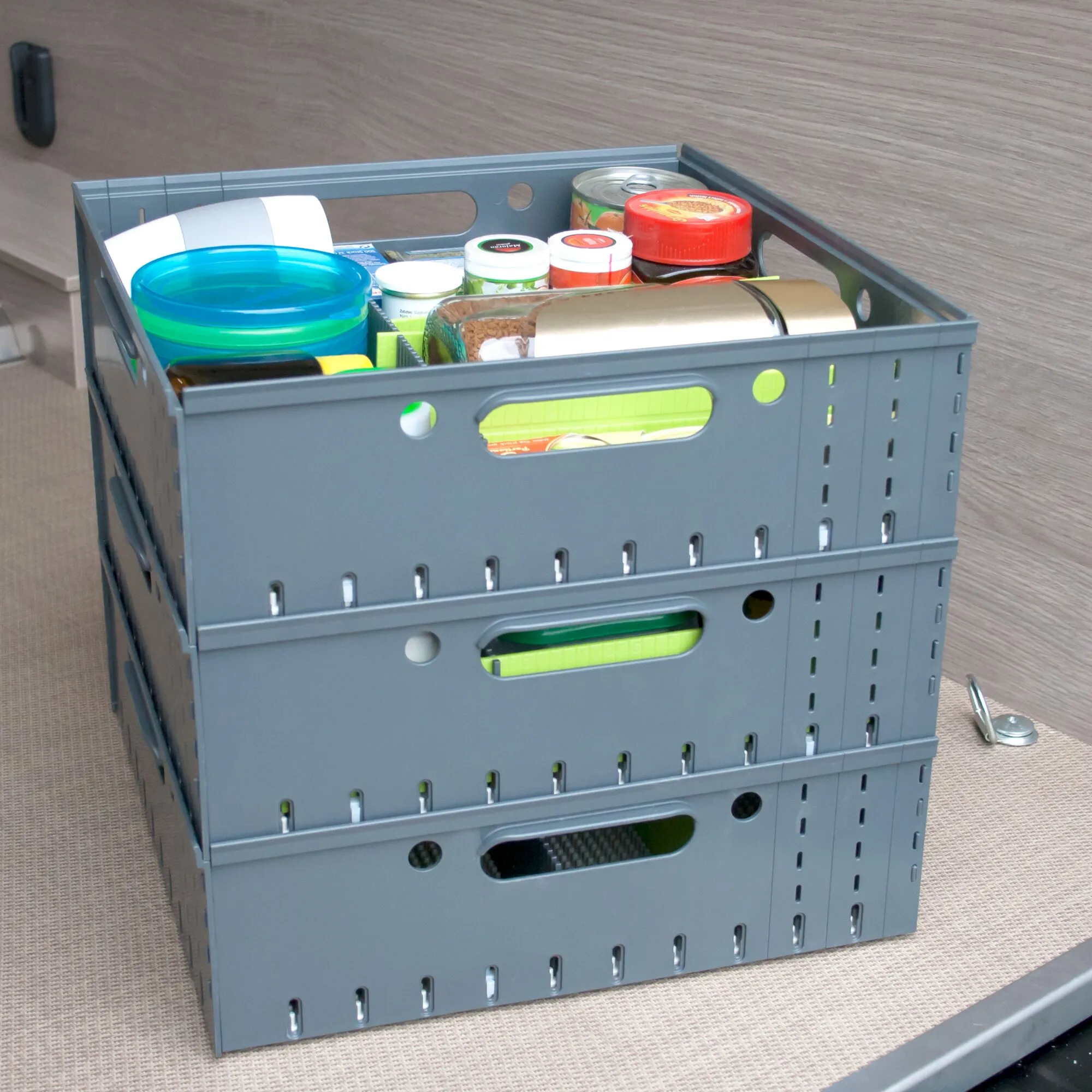 Dreistöckiger grauer Stau-Tower aus faltbaren Kunststoffboxen, die oberste Box ist mit Vorräten und Haushaltsgegenständen gefüllt