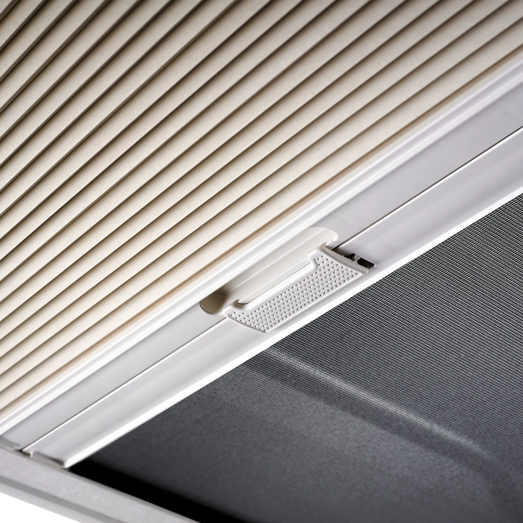 Detailansicht des Dachfensters Heki 2 de Luxe mit cremefarbenem Plissee, weißem Rahmen und perforiertem Griffbereiche