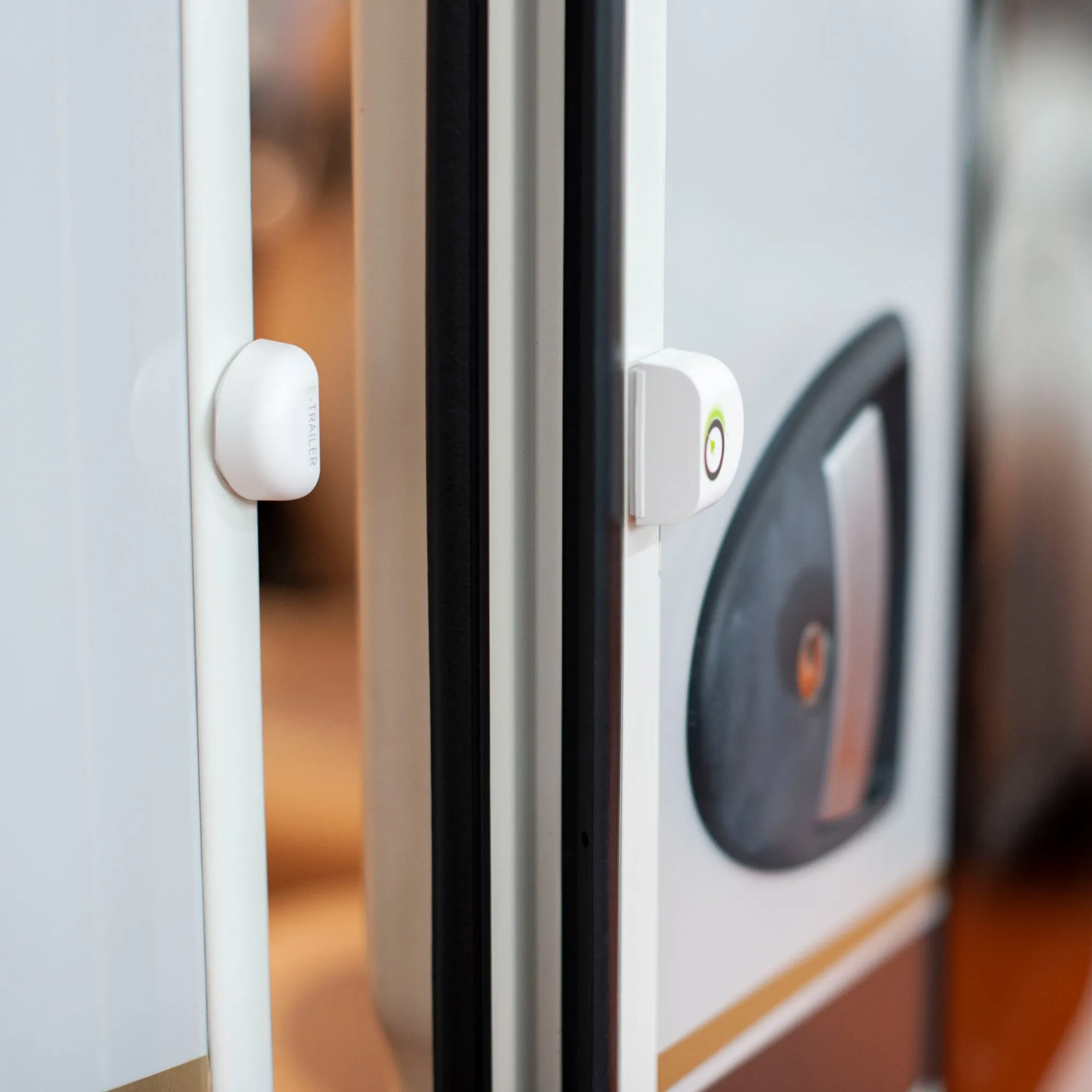 Weißer E-Switch Tür- und Fenstersensor an einem geöffneten Fenster mit sichtbarer Waschmaschine im Hintergrund