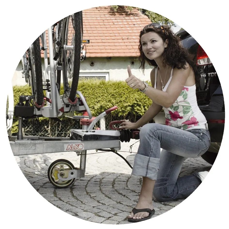 Frau befestigt ein Stützrad Premium an einem Fahrradträger auf der Anhängerkupplung eines Autos