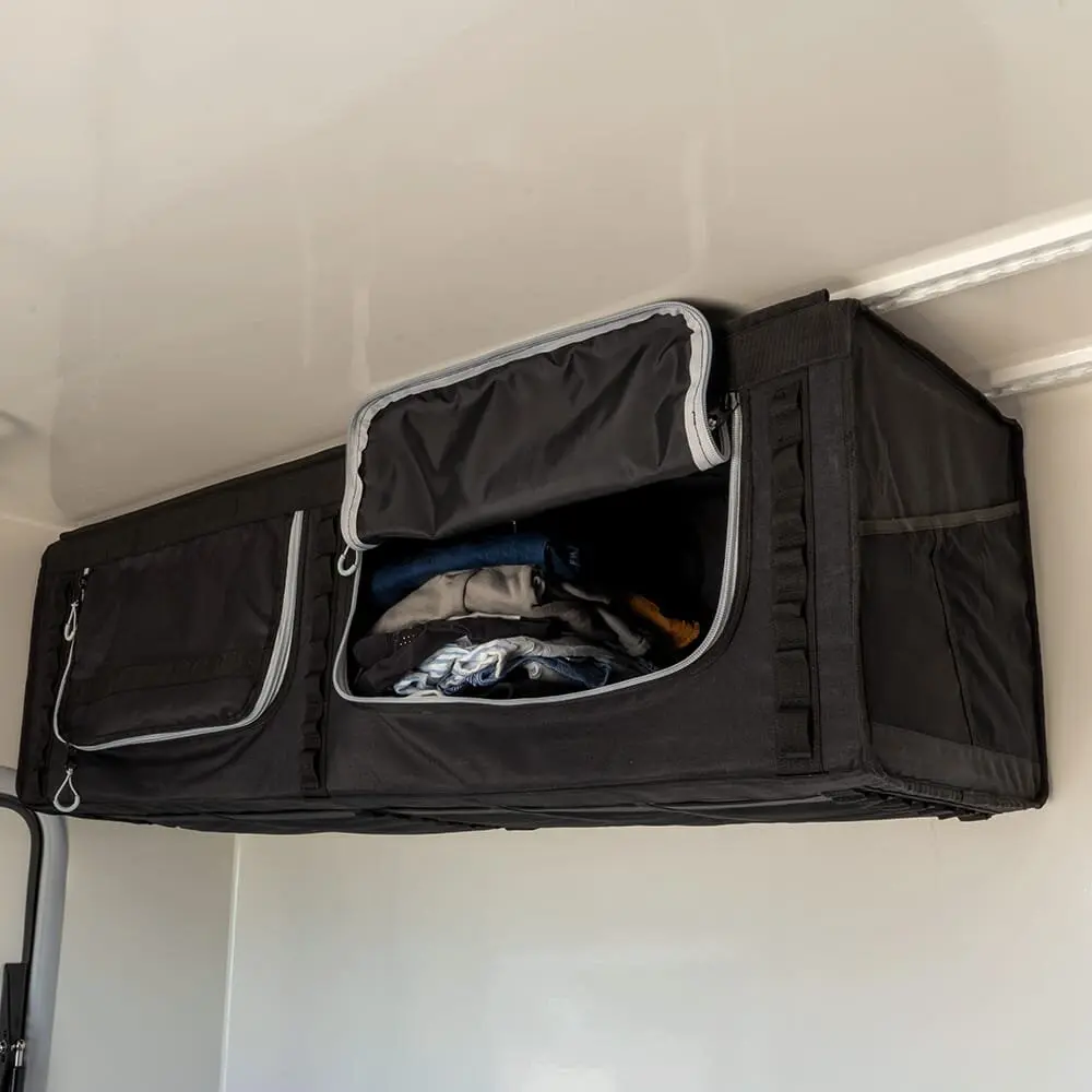 Schwarzes Staufach wallBOXX L aus Stoff, an der Wand montiert, mit geöffnetem Fach voller Kleidung und seitlichen Reißverschlusstaschen