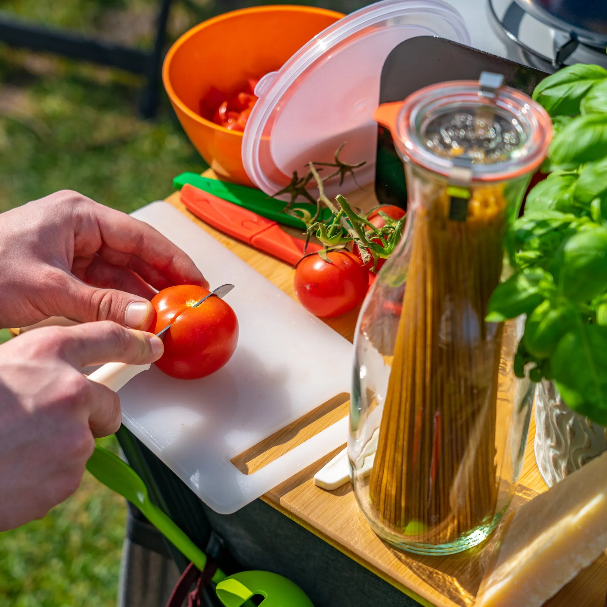 Schneidebrett-Set aus weißen Kunststoff- und Bambusbrettern beim Schneiden einer Tomate mit weiteren Küchenutensilien und Gemüse