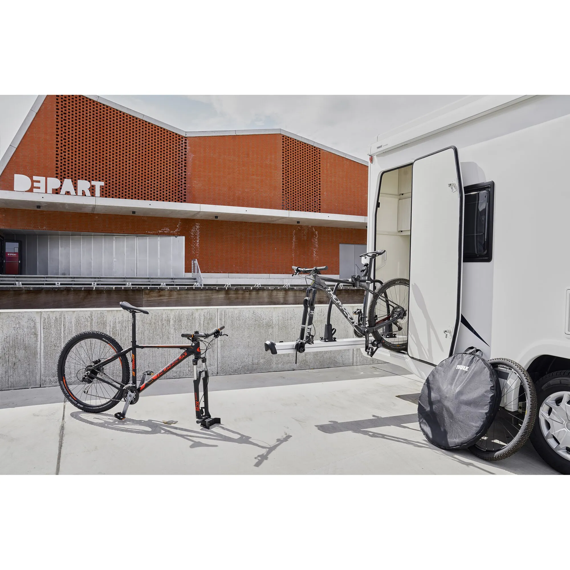 Fahrradträger mit Thule Gabelmontage-Adapter an einem weißen Wohnmobil, zwei Mountainbikes und Laufradtasche sichtbar