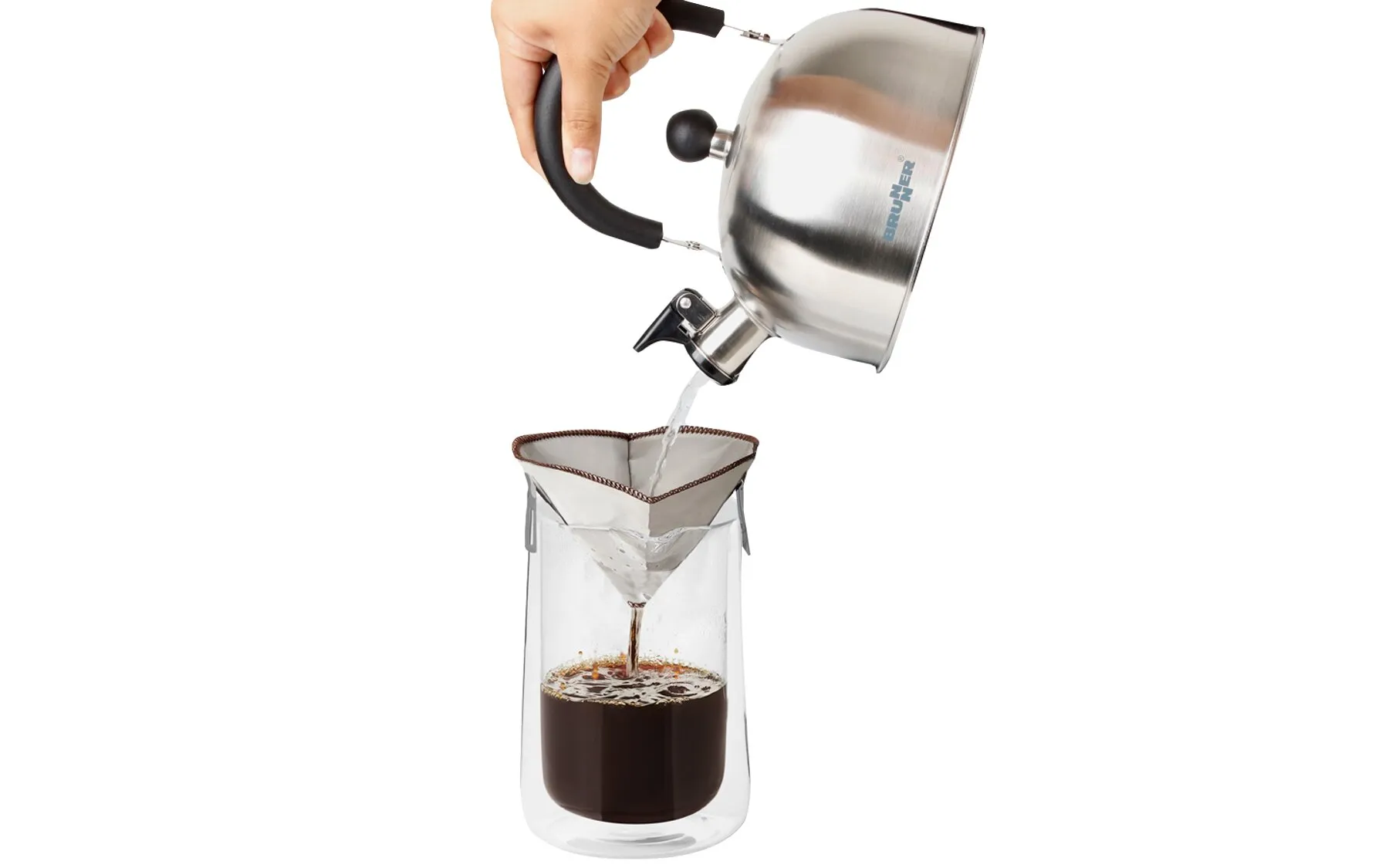 Hand hält einen Edelstahlkessel und gießt heißes Wasser durch den Kaffeefilter Amigo in eine Glaskanne mit Kaffee