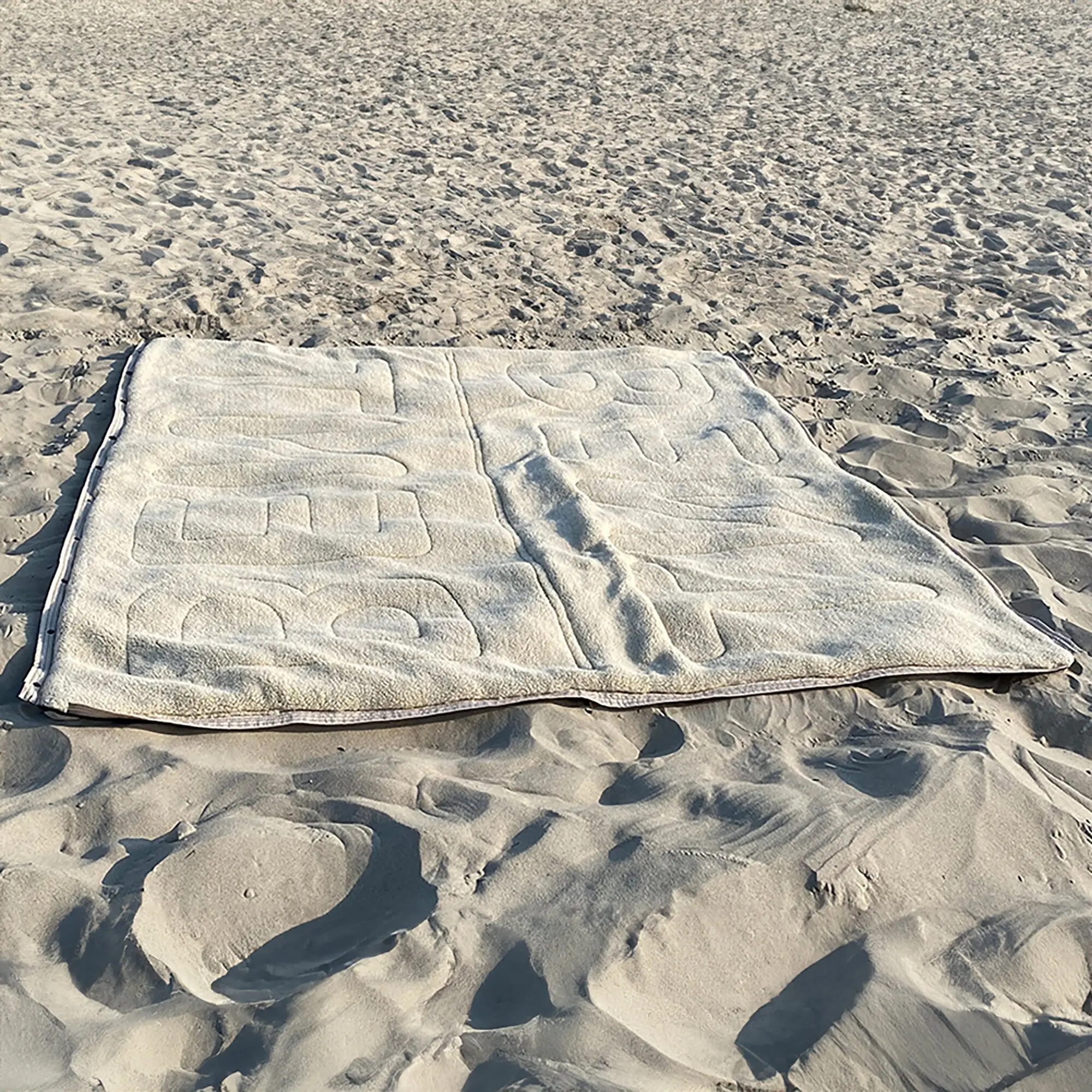 Heller Vanlife Schlafsack Bentcho mit quiltartiger Steppung liegt flach auf Sand am Strand; seitlicher Reißverschluss sichtbar