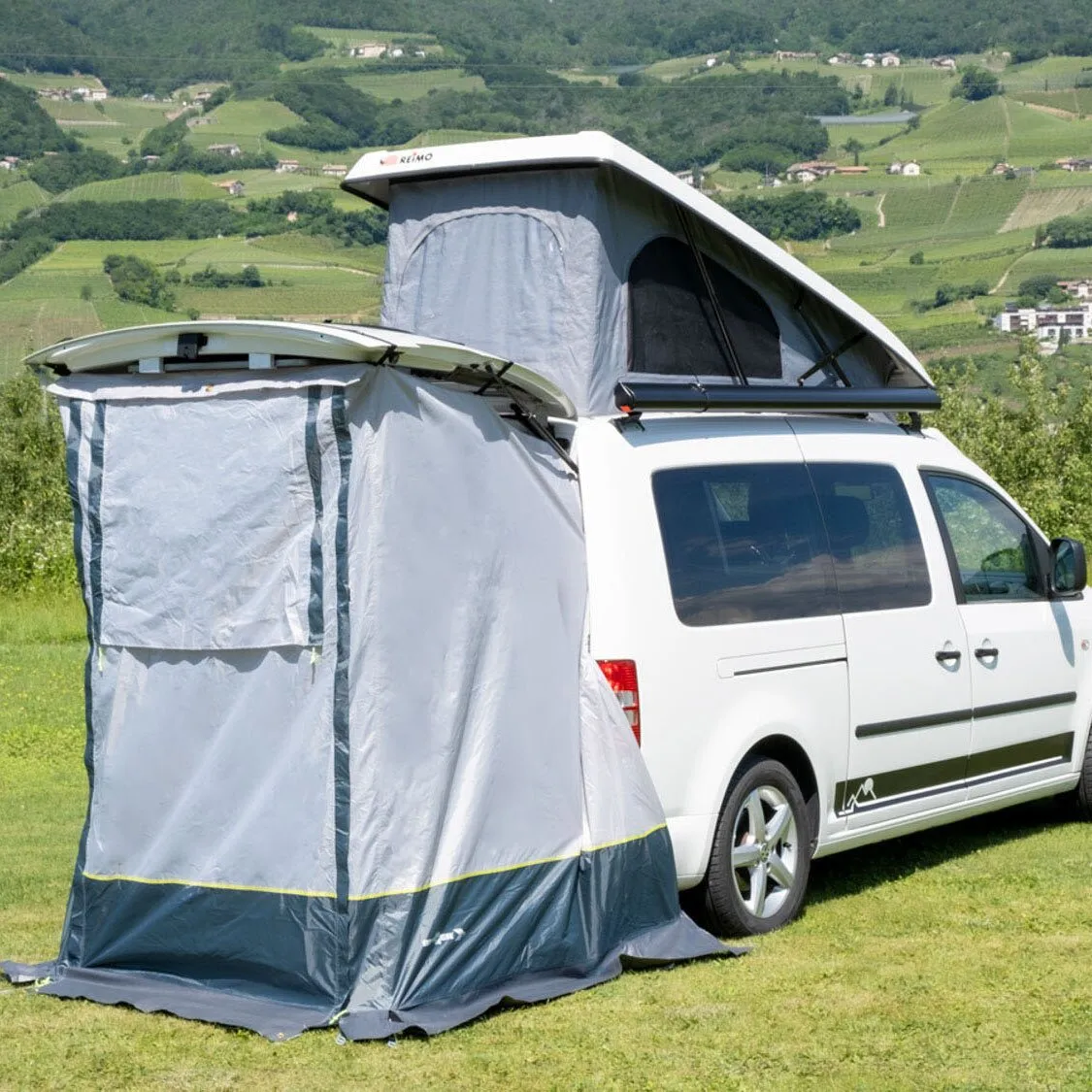 Graues Heckzelt Pilote Caddy 4 an einem weißen VW Caddy mit geöffnetem Dachzelt auf einer Wiese vor Weinbergen
