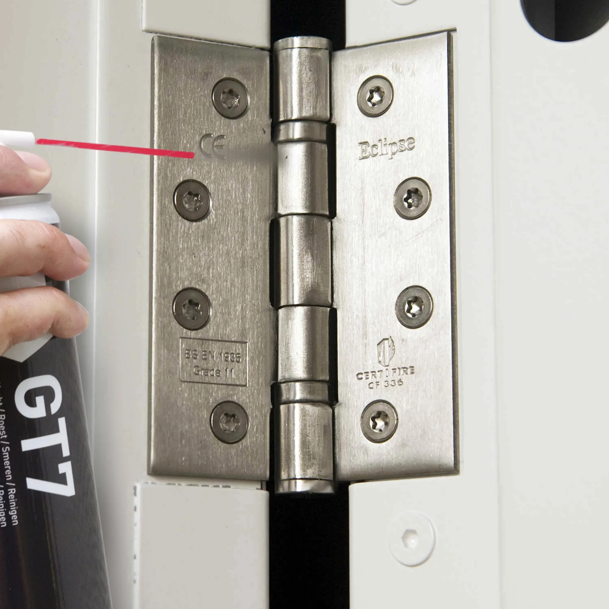 GT7 Multifunktionsspray wird mit rotem Sprührohr auf ein Edelstahl-Türscharnier mit Schrauben aufgetragen