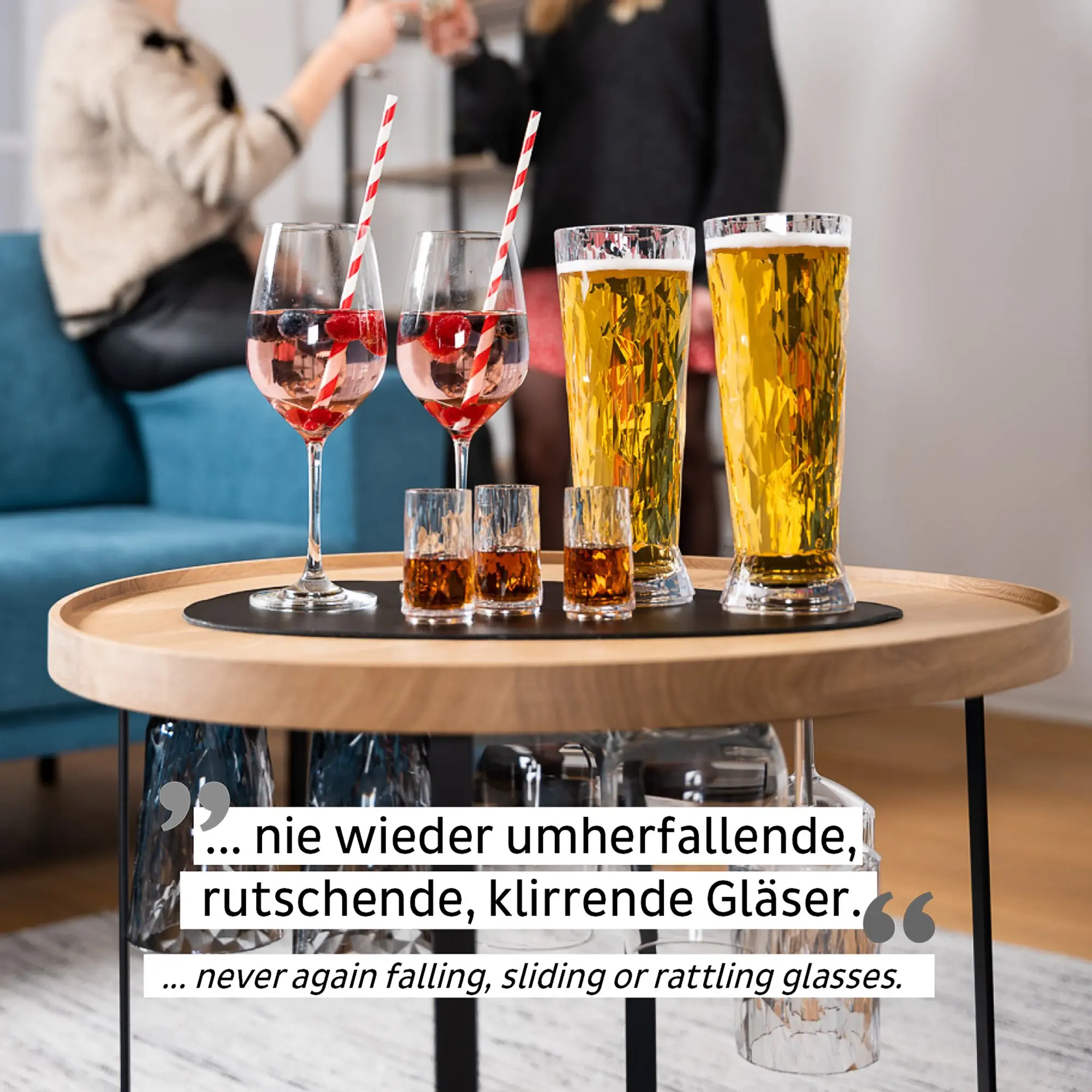 Runder Holztisch mit mehreren Gläsern: zwei Weingläser mit rosa Getränk und rot-weißen Strohhalmen, zwei hohe Gläser mit goldener Flüssigkeit; darunter eine runde schwarze Platzunterlage aus Metall-Nano-Gel, Hintergrund unscharfe Personen