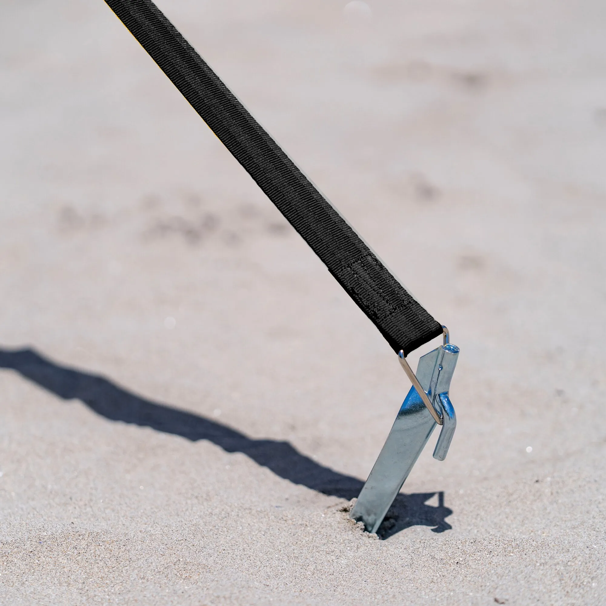 Schwarzes Abspannband Tie Down S mit Metallspanner, im Sand an einem Bodenanker befestigt