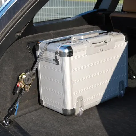 Silberner Hartschalenkoffer im Kofferraum, mit einem Zurrgurt Auto Cargo Belt an der Seitenwand befestigt
