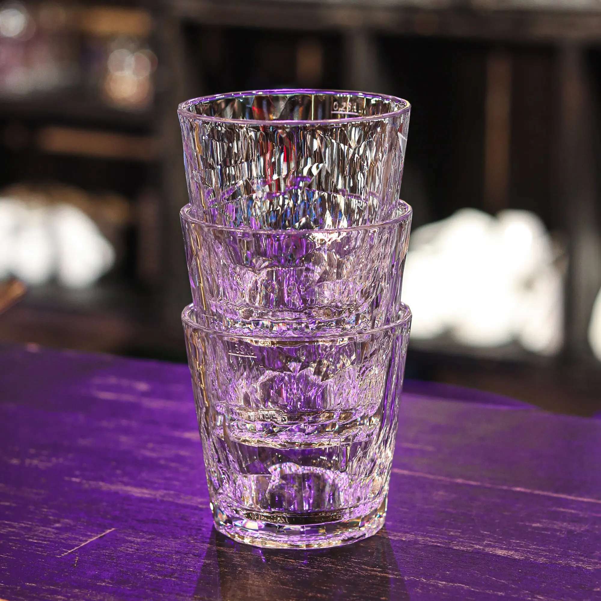 Mehrere transparente Trinkgläser Superglas CLUB mit geriffelter Oberfläche, übereinandergestapelt auf violett beleuchteter Fläche