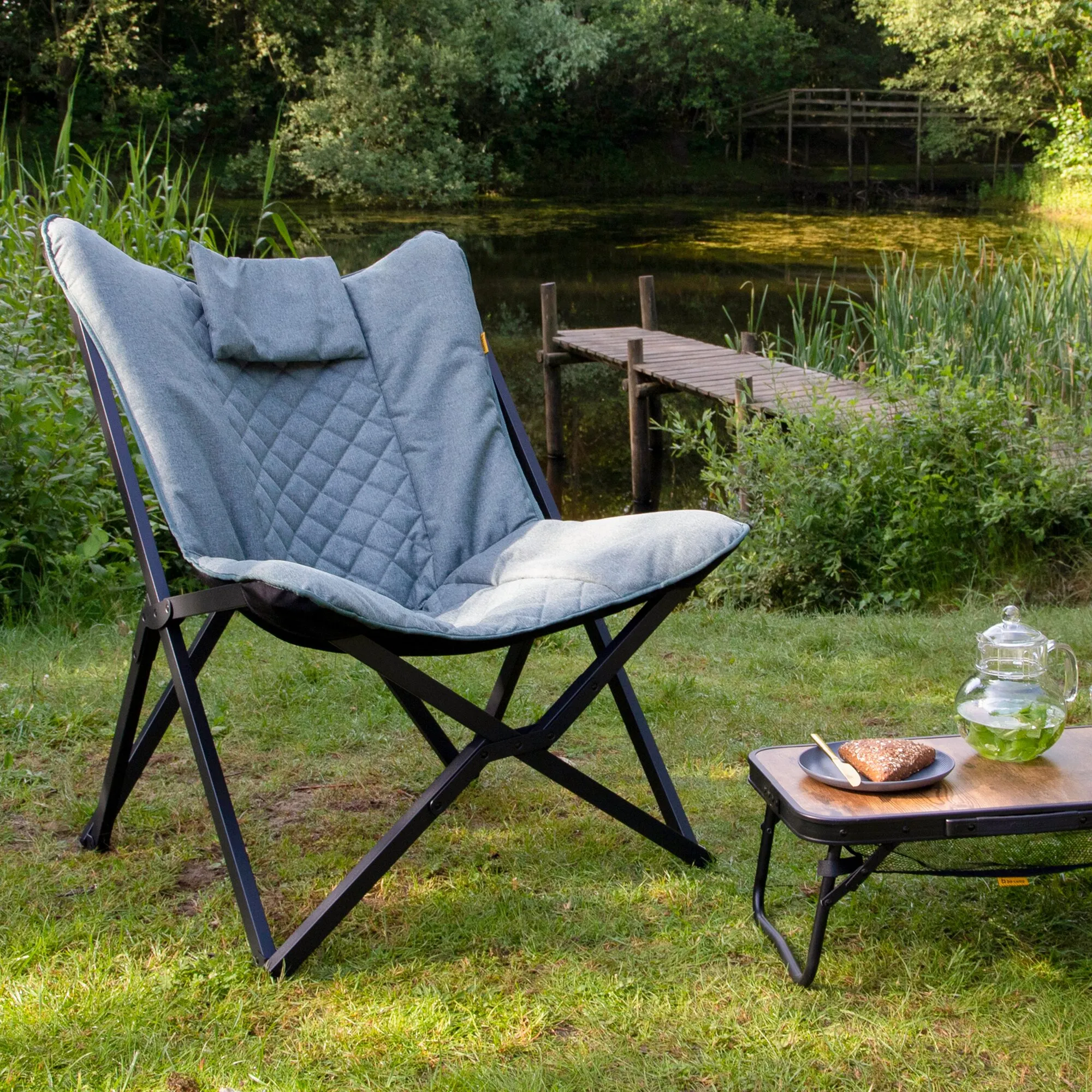 Relaxsessel Molfat XL mit hellgrauem, gestepptem Polster und schwarzem Klappgestell am Gartenteich neben Beistelltisch und Getränk